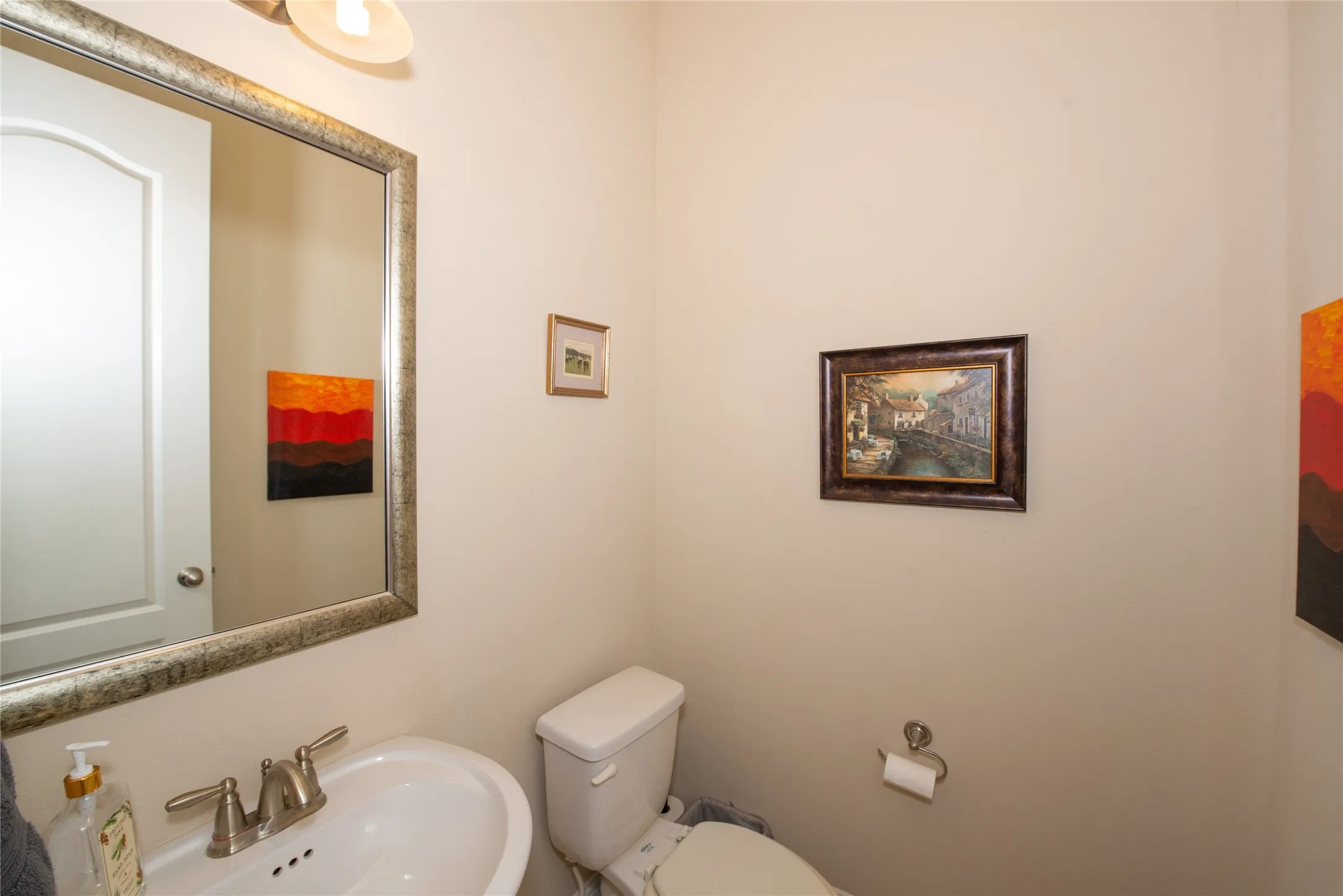 Pedestal sink with brushed nickel faucet, wall-mounted mirror with an ornate frame, and a flush toilet