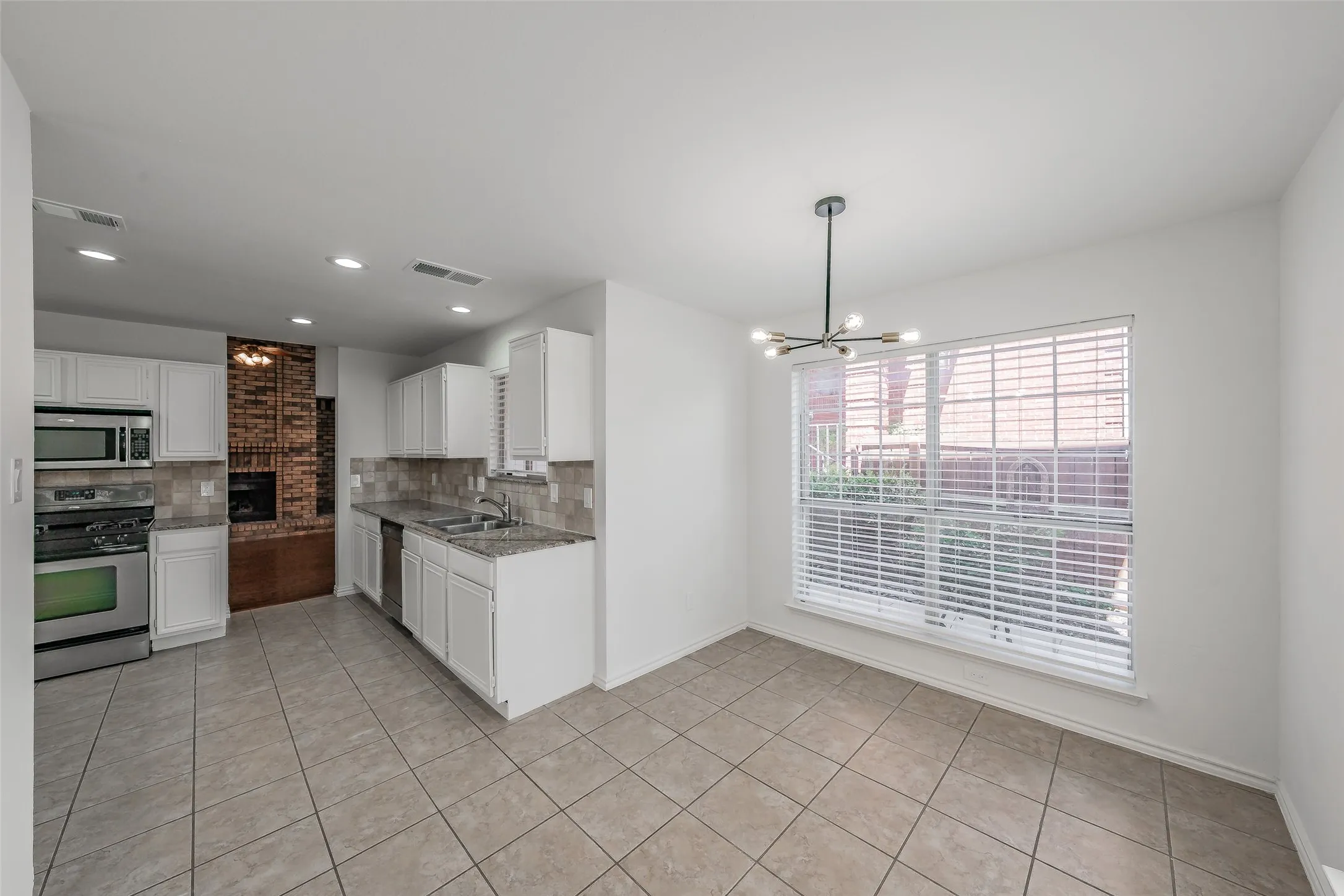 Kitchen and dining area featuring tile flooring, white cabinetry, stainless steel appliances, and a modern chandelier