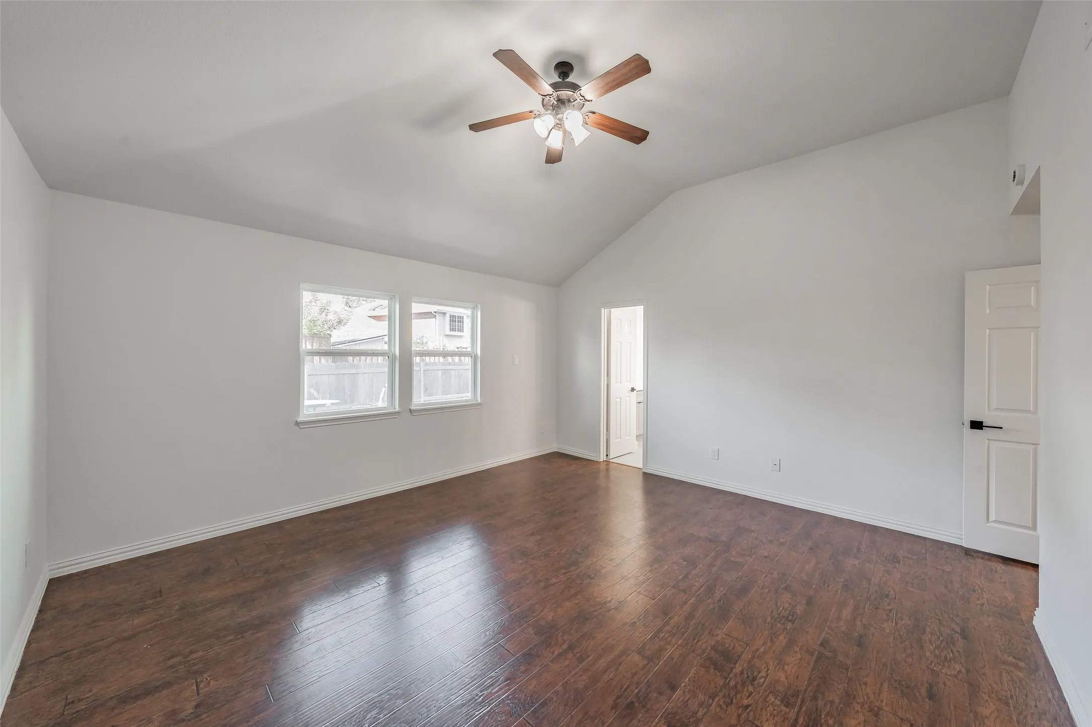 First floor primary bedroom has vaulted ceiling with a ceiling fan, wood flooring, and large windows and white interior walls