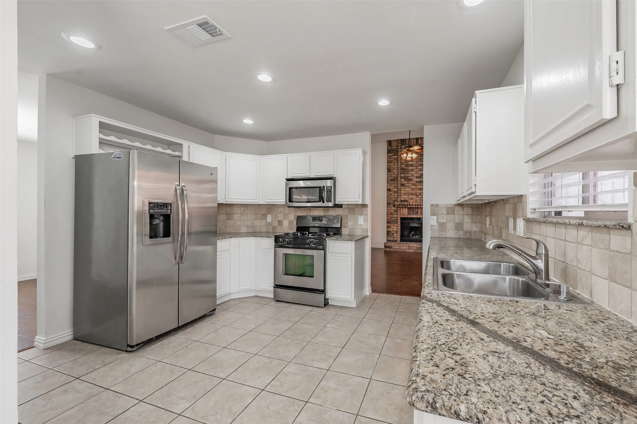 Kitchen featuring tile flooring, white cabinetry, stainless steel appliances, granite countertops, and a tile backsplash