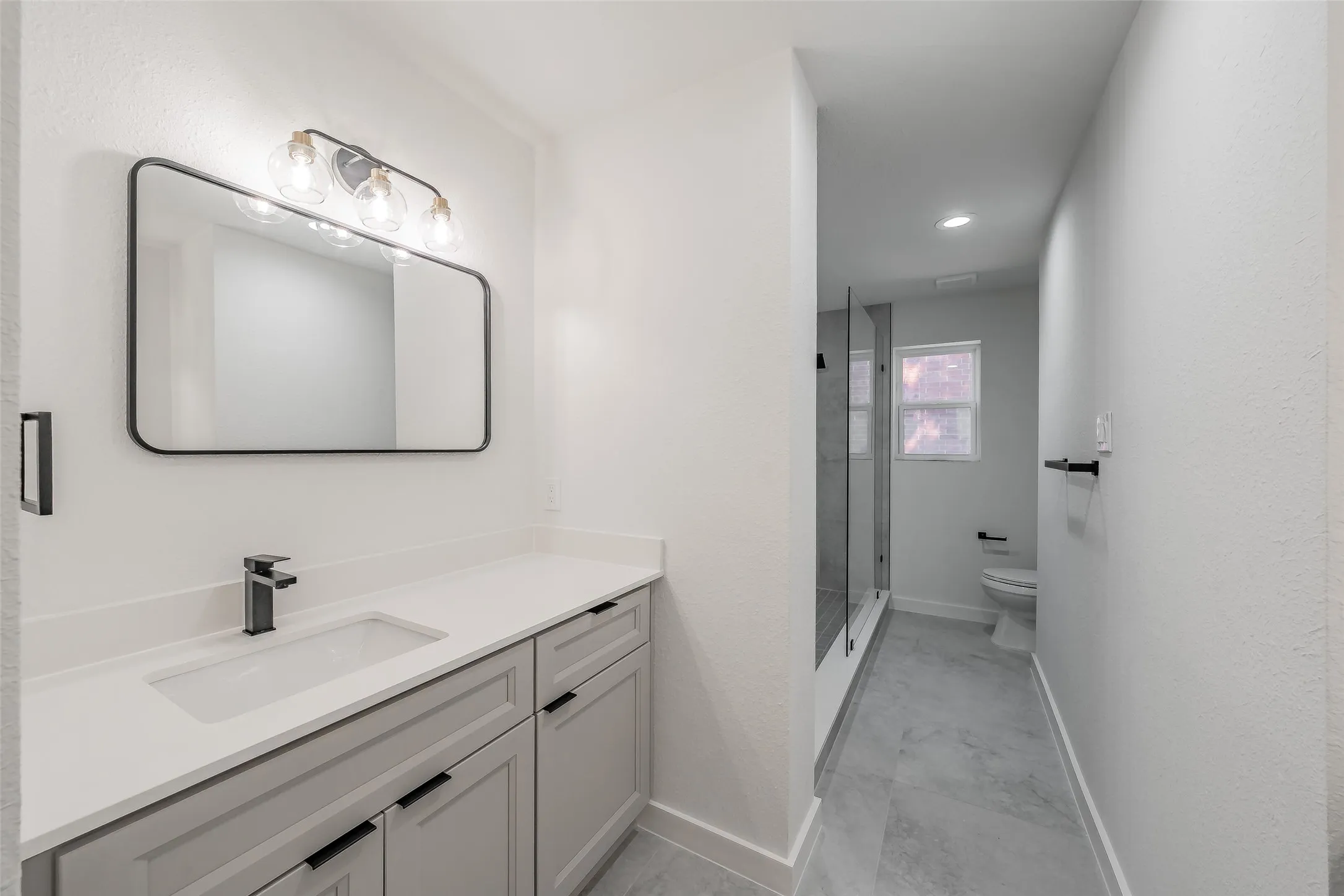 Second vanity with an integrated rectangular sink, matte black faucet, and light gray cabinetry leads to oversized shower and private toilet area