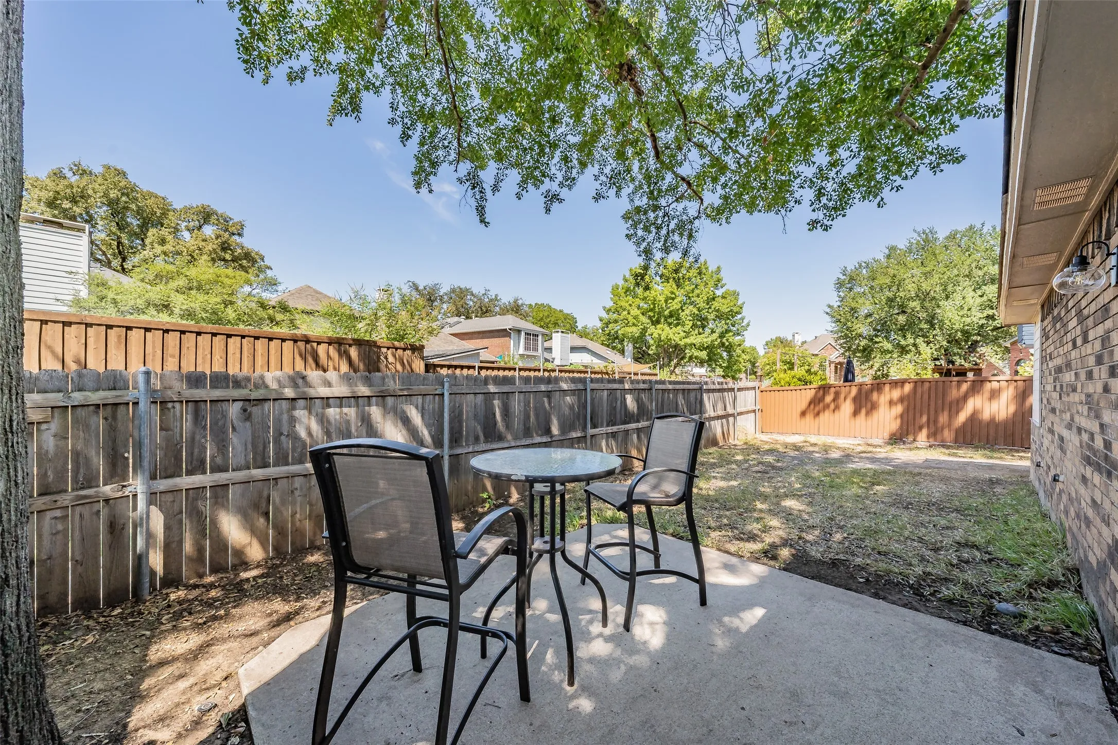 Expansive backyard featuring a concrete patio, wood privacy fencing, and mature trees