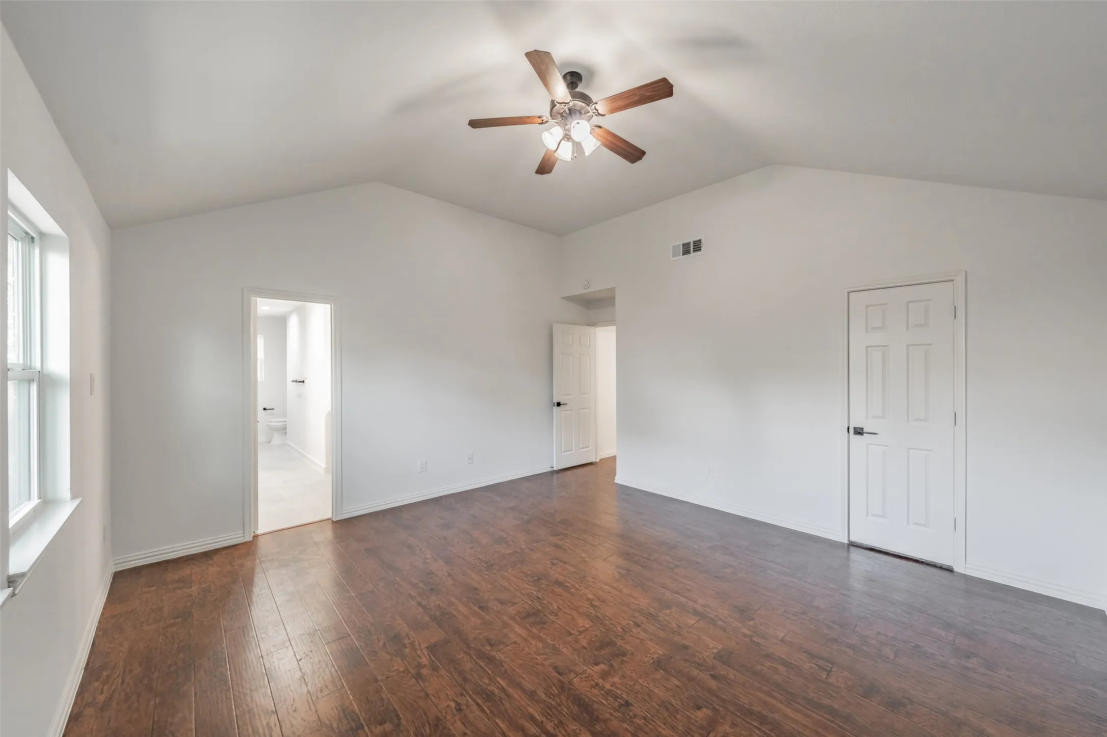 Vaulted ceiling with a ceiling fan, wood-finish flooring, and white paneled doors