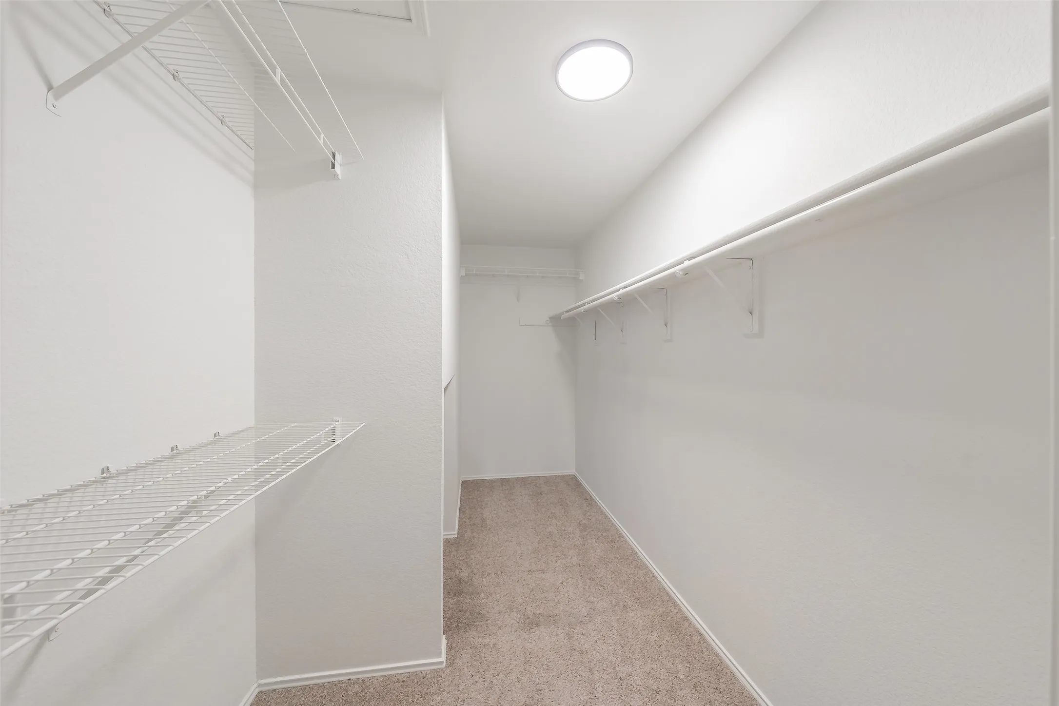 Recessed ceiling light fixture, white wire shelving, white walls, and neutral carpet