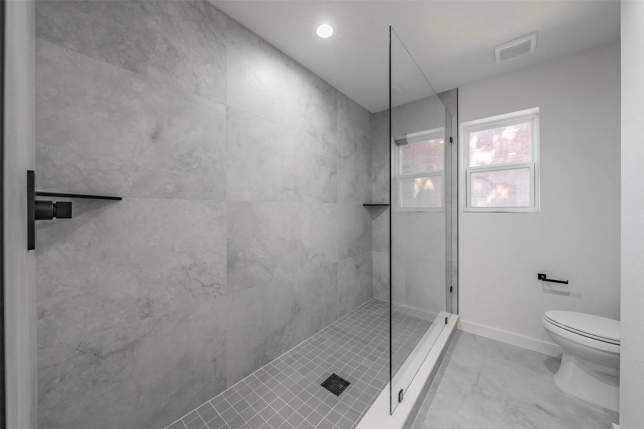 Glass-enclosed oversized shower with large format wall tiles, a built-in shower niche, and a tiled floor