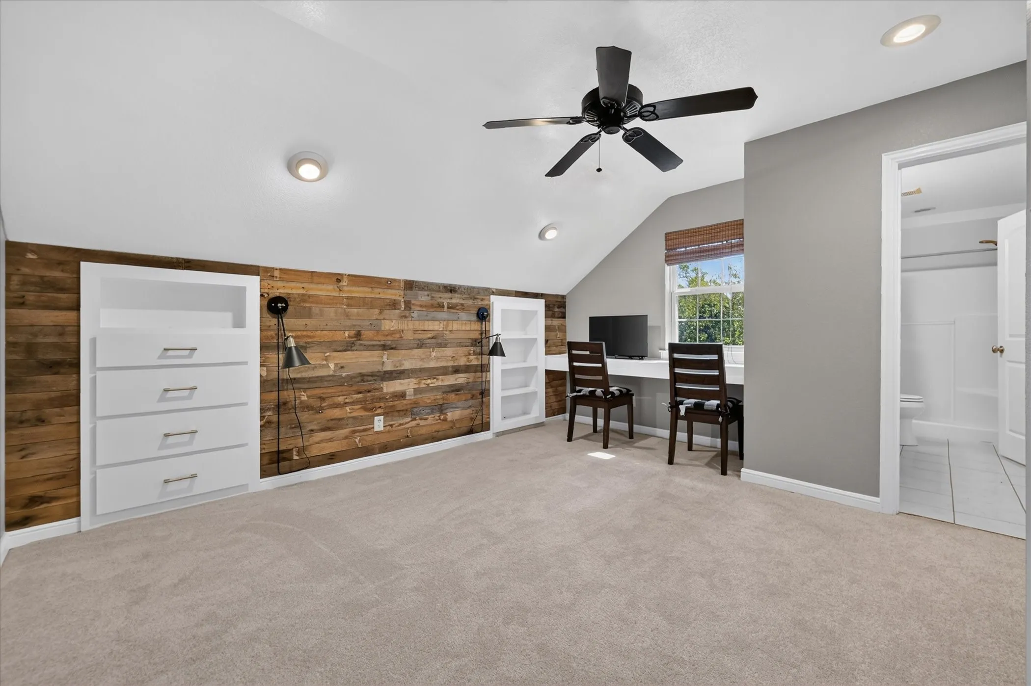 Carpeted room featuring a wood-panel accent wall, built-in storage, a built-in desk, and a ceiling fan