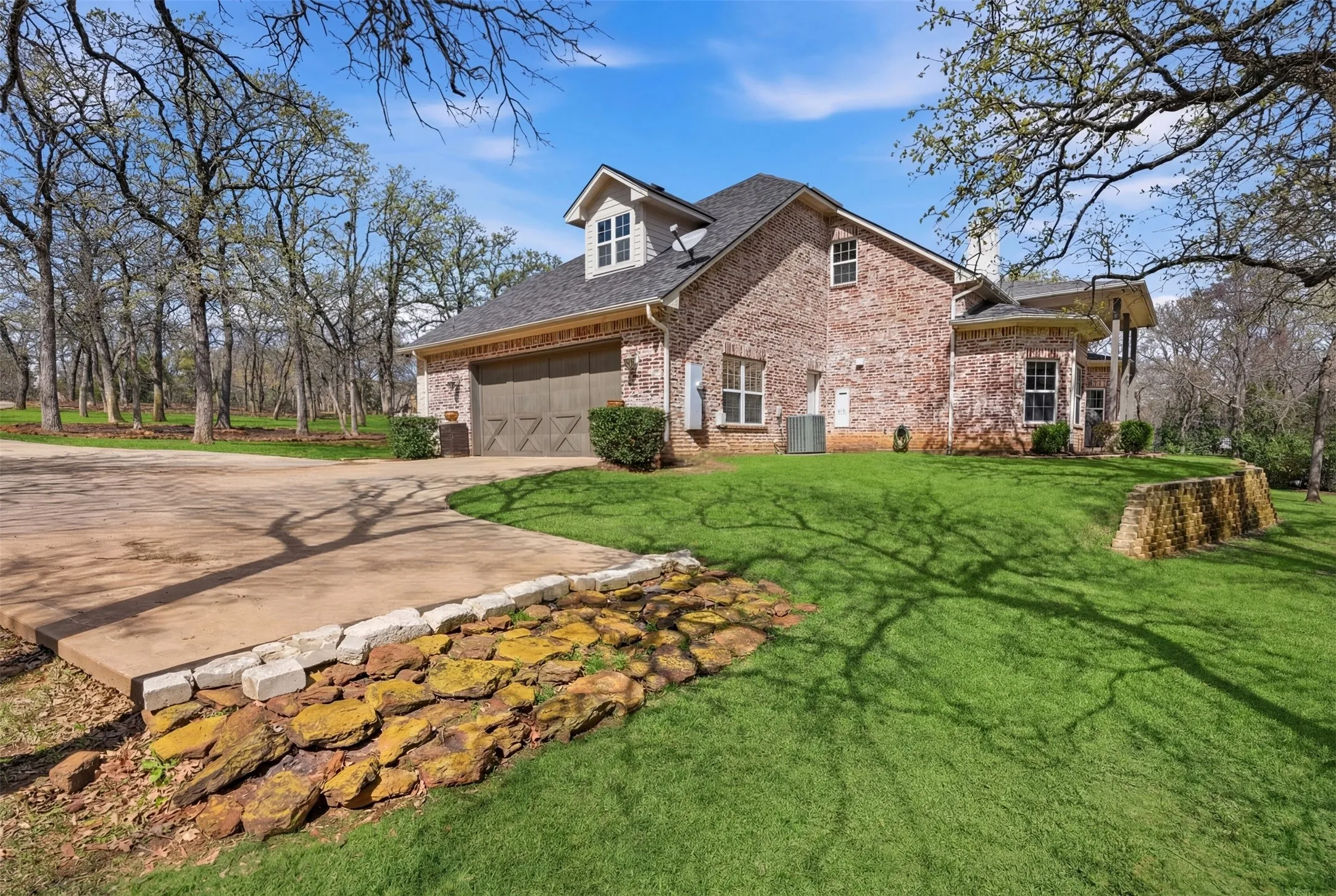 Brick exterior, dormer window, attached garage with decorative door, concrete driveway, and manicured lawn