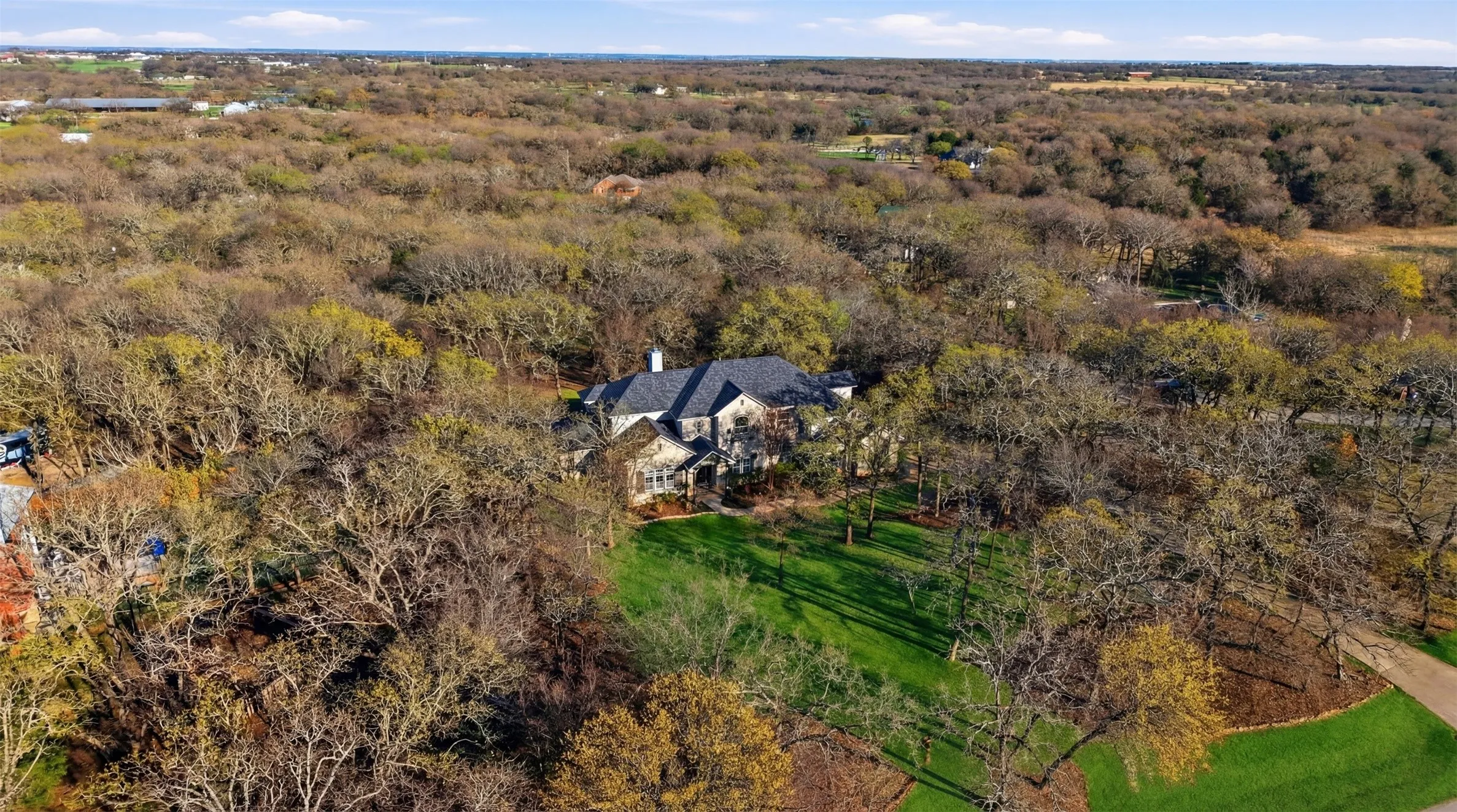 Expansive property featuring a stone exterior residence, a dark-toned roof, and extensive surrounding woodland
