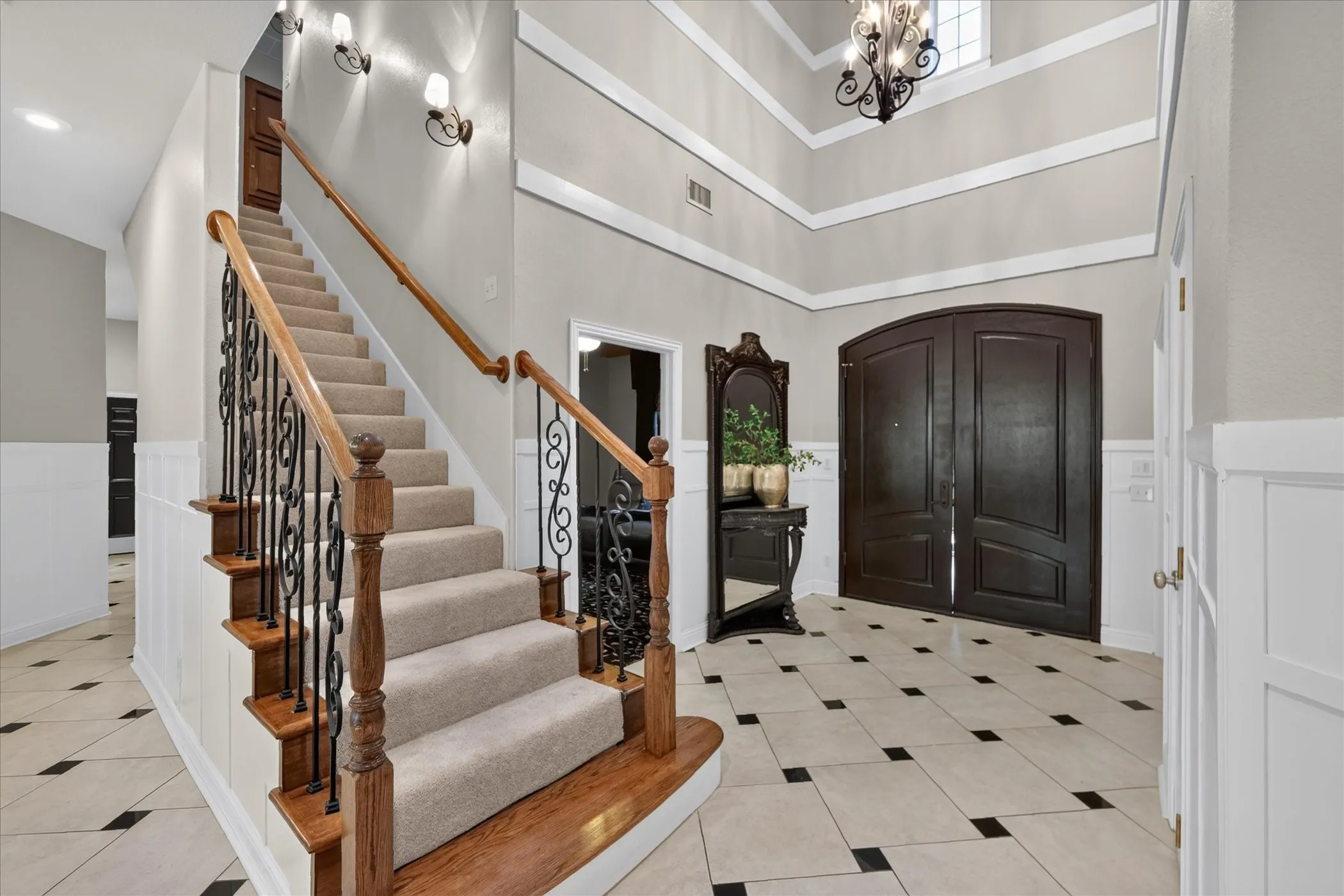 Grand entry featuring a two-story ceiling, wood and wrought iron staircase, patterned tile flooring, and wainscoting