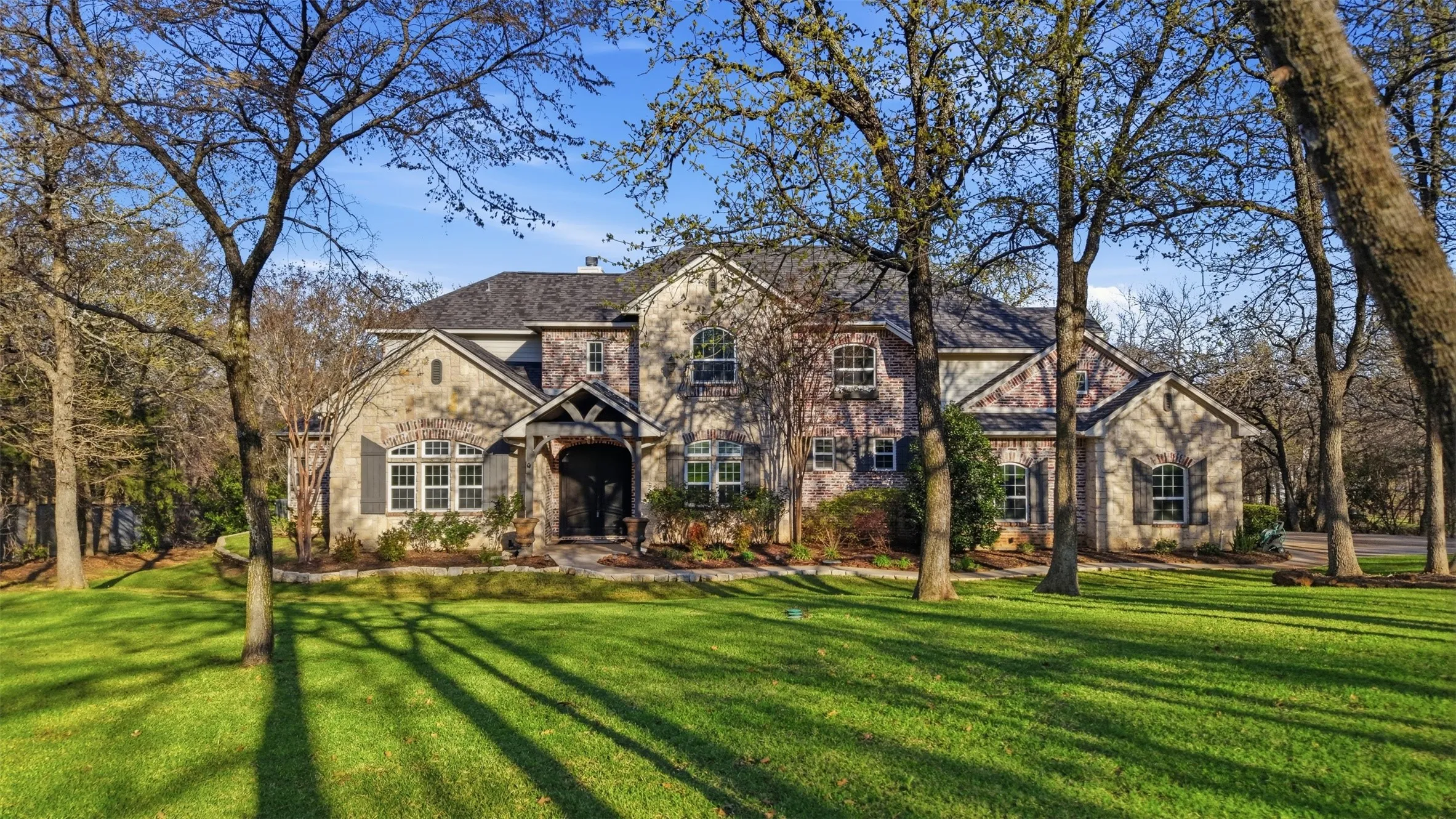 Expansive green lawn with mature trees and a multi-textured stone and brick facade