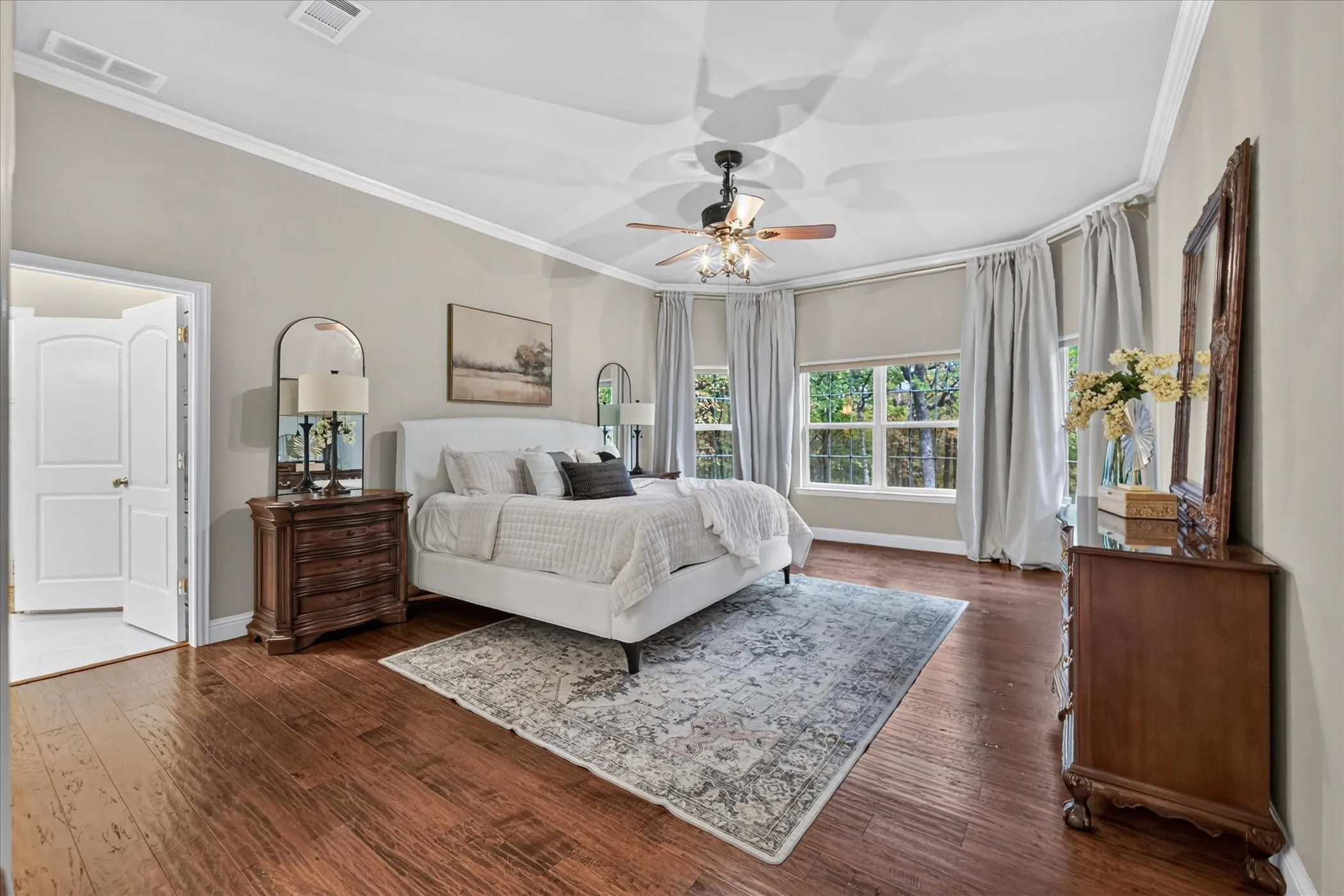 Wood-finish flooring, recessed ceiling with crown molding, ceiling fan with integrated lighting, multiple windows with roller shades, and double-entry doors