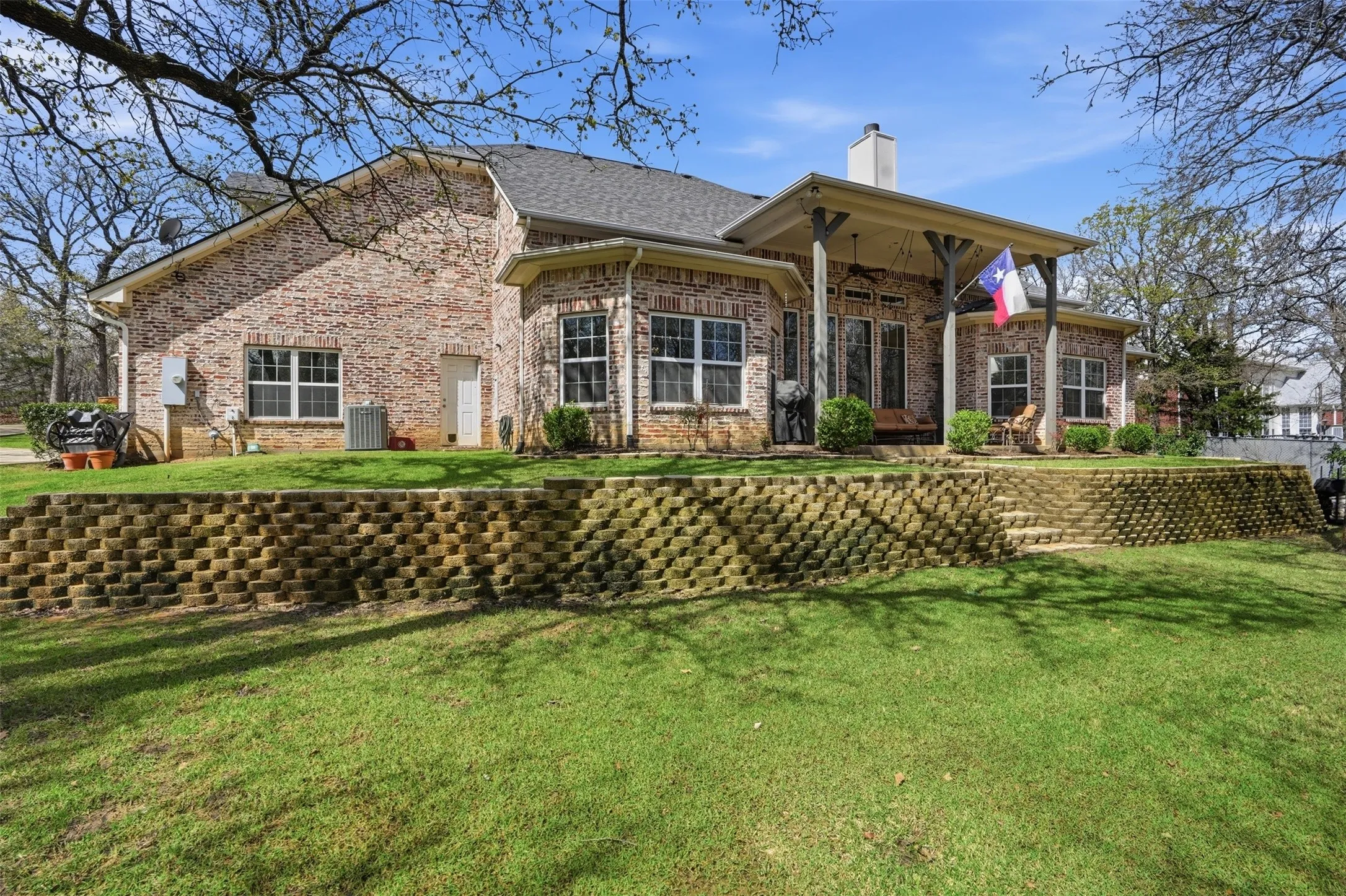 Brick exterior, covered patio, raised patio, built-in retaining wall, and established landscaping