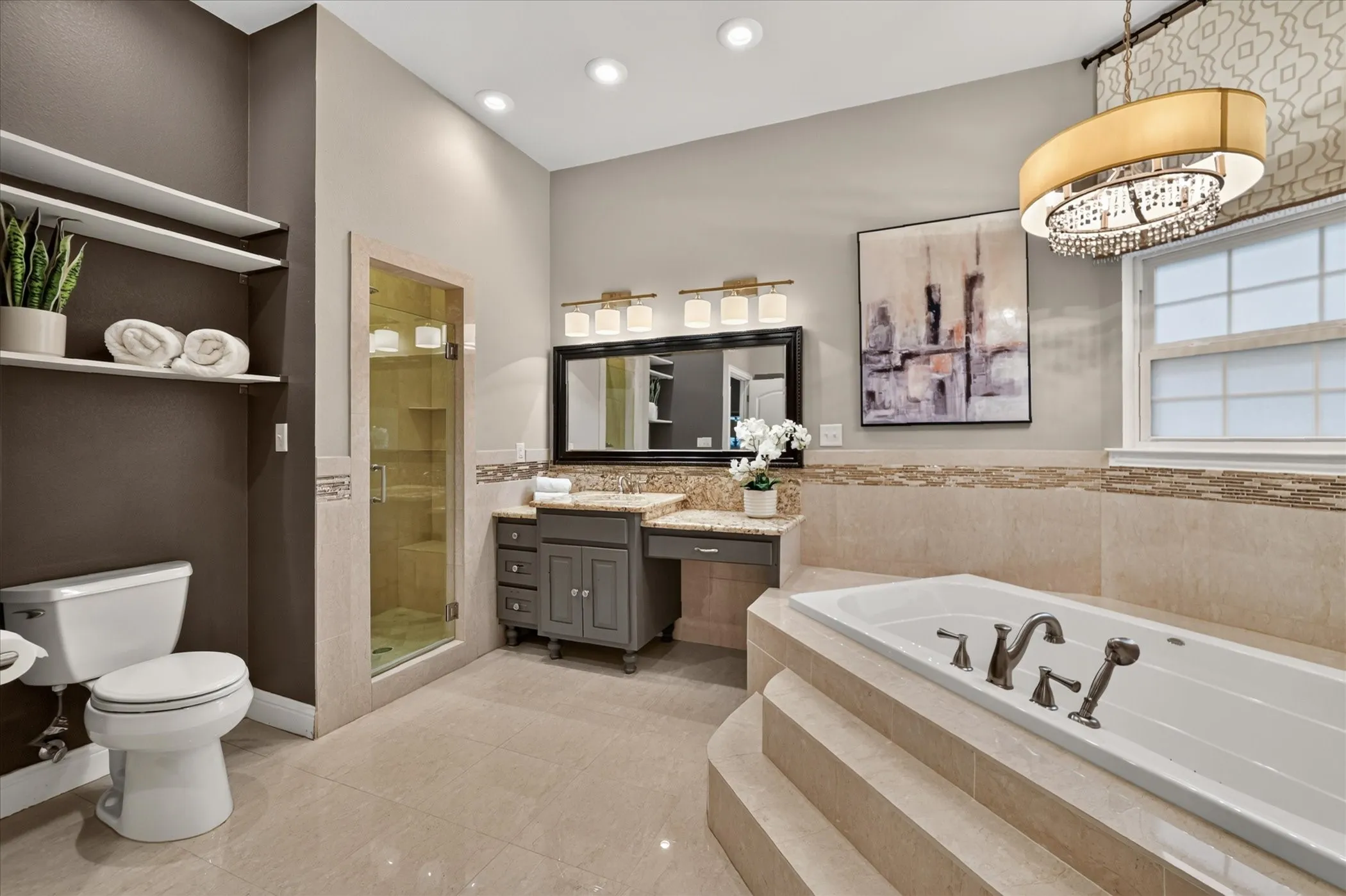 Deep soaking tub with tiled surround, glass-enclosed shower, vanity with stone countertop, recessed lighting, and a decorative chandelier