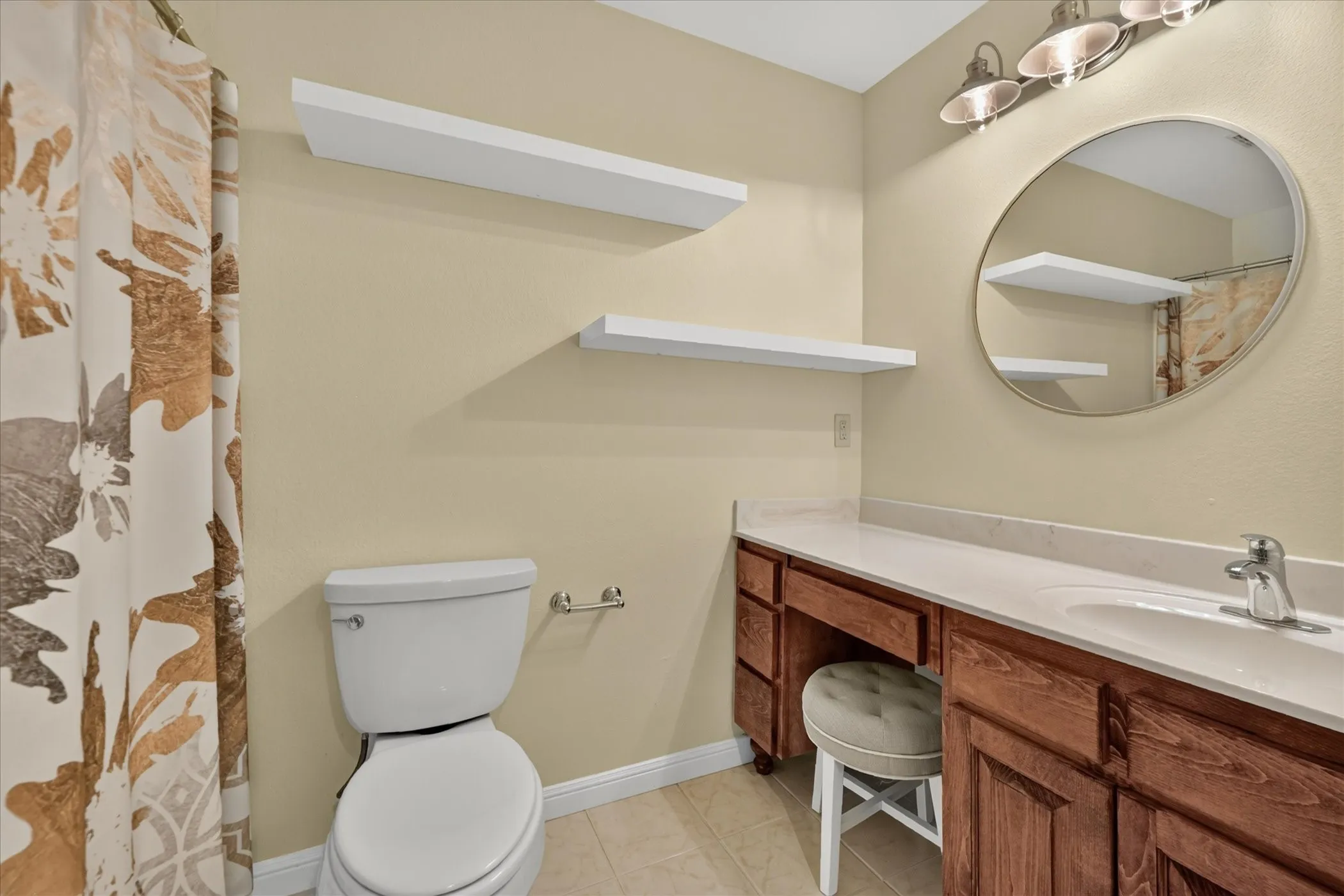Bathroom featuring a single vanity with a built-in makeup area, a circular mirror, and a three-light fixture