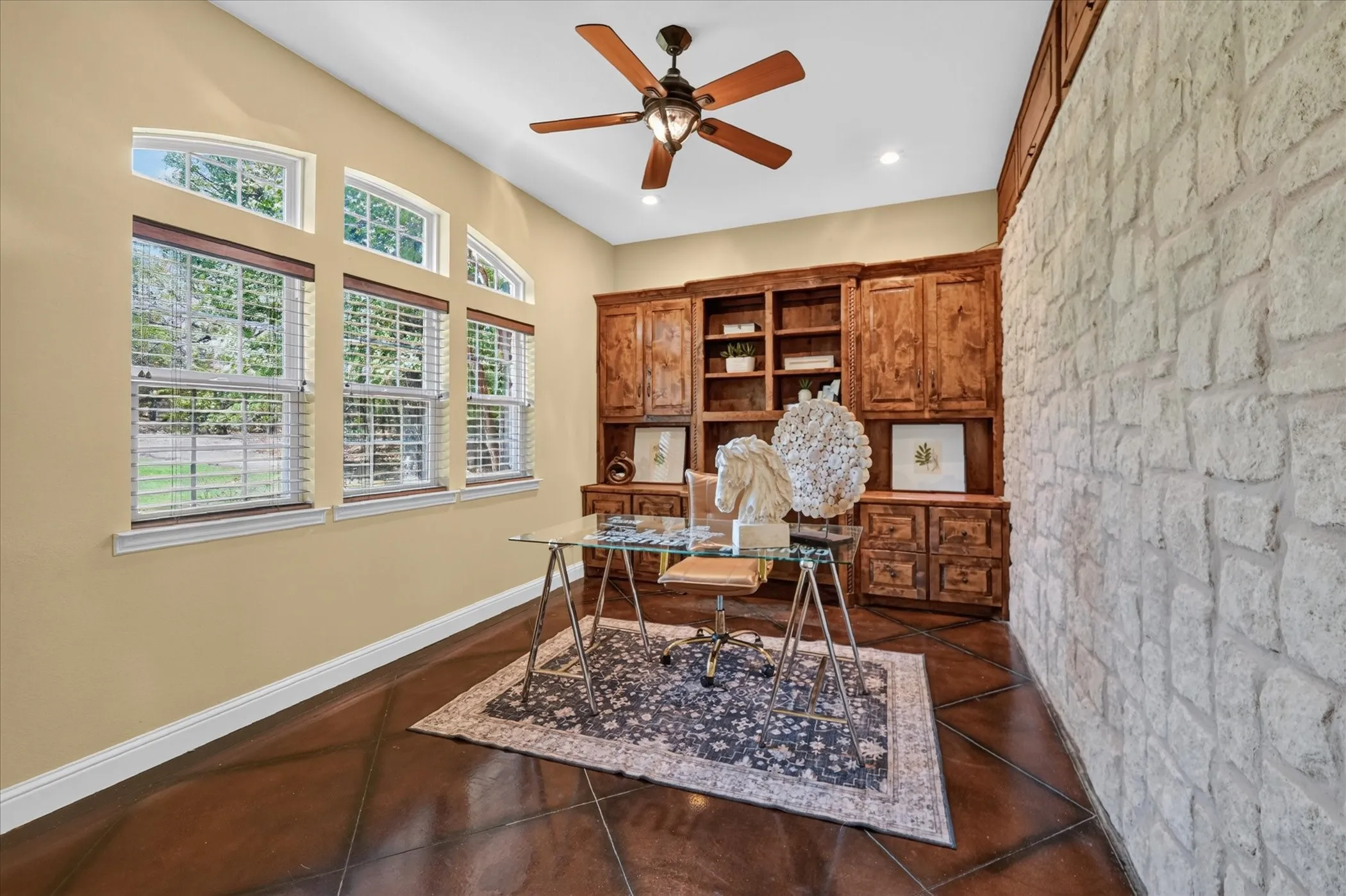 Arched windows, built-in wooden cabinetry, stone accent wall, ceiling fan, and recessed lighting
