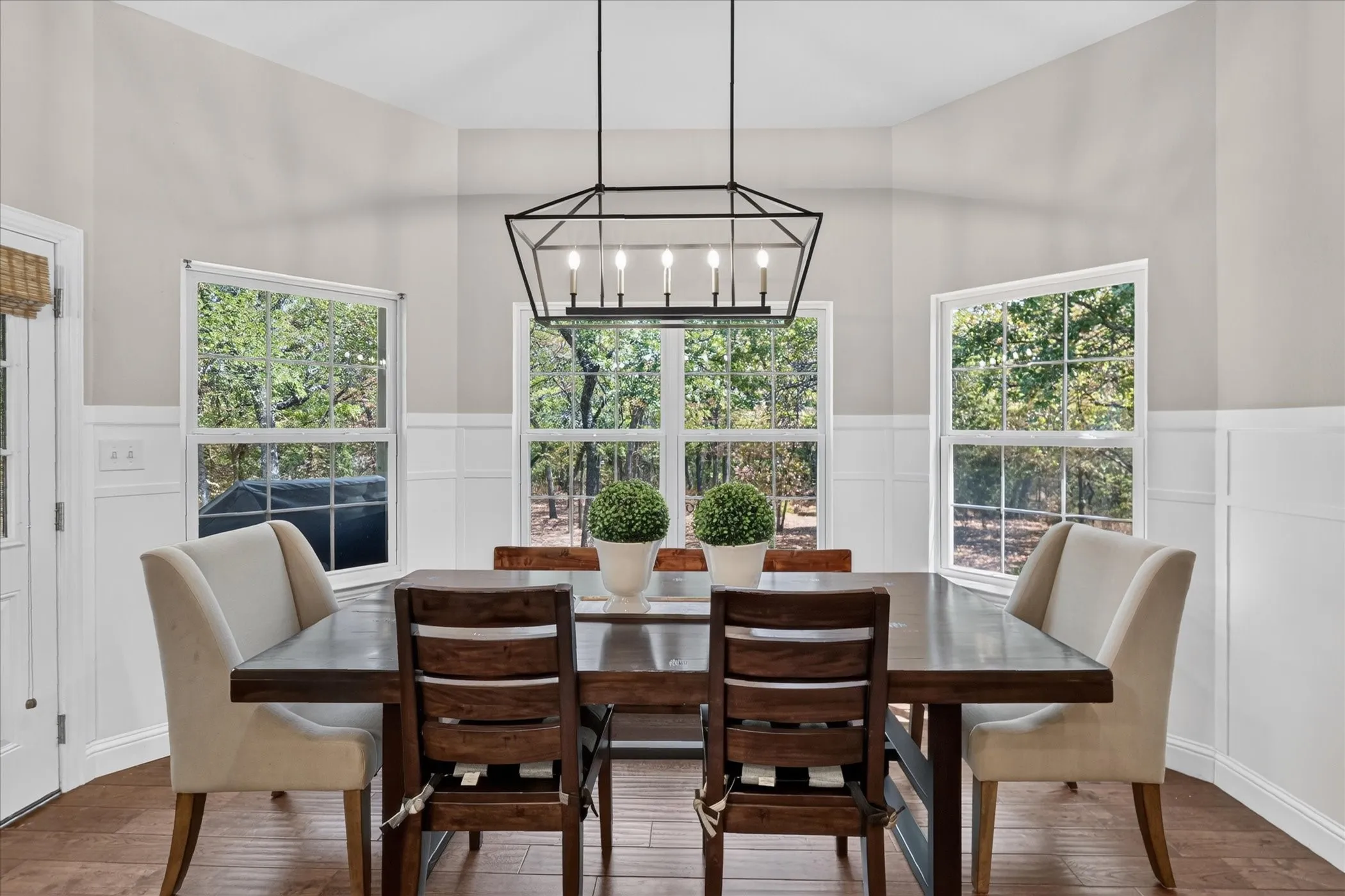 Vaulted ceiling with a geometric chandelier, multiple windows, wood-finish flooring, and white wainscoting