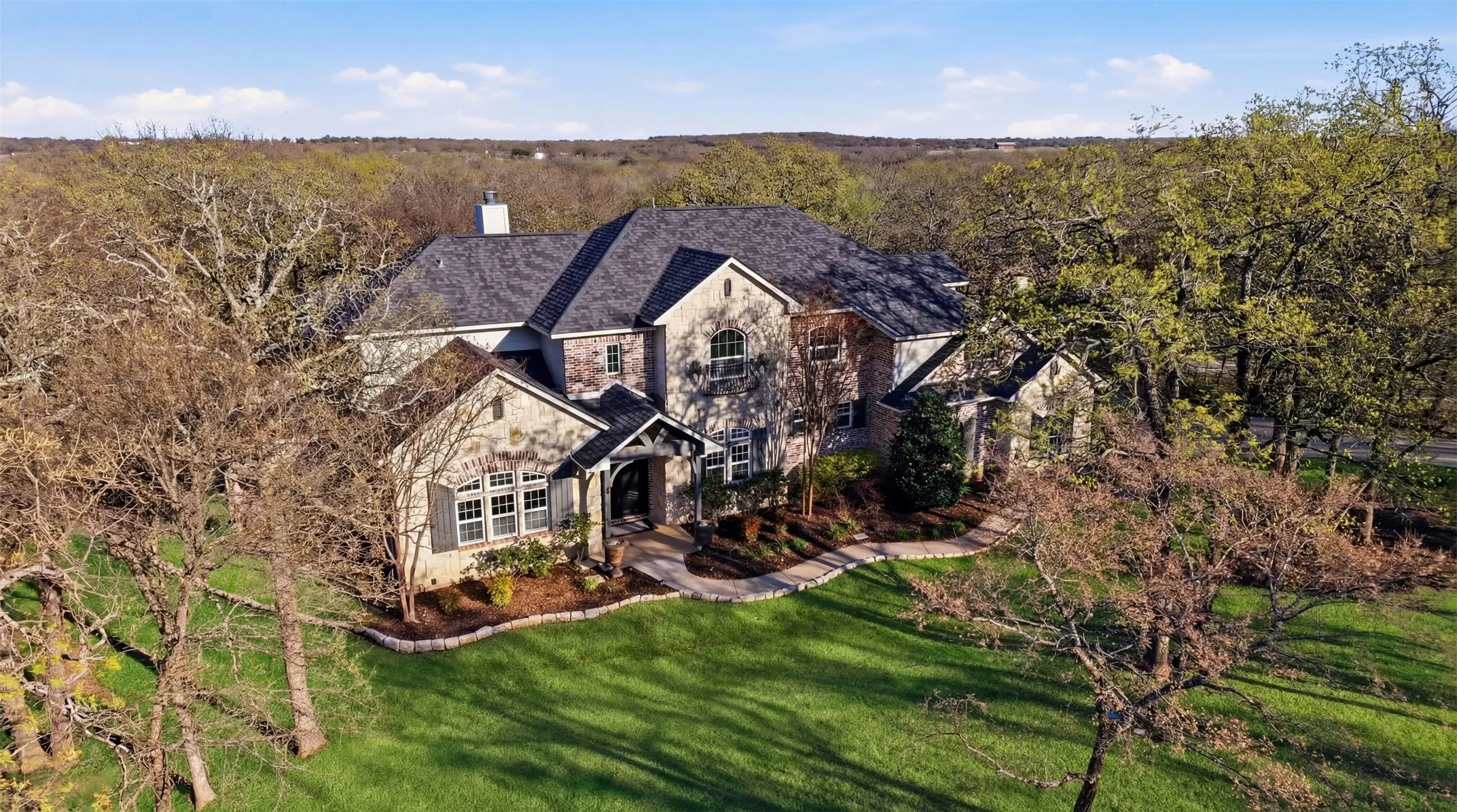 Stone exterior with dark shingle roof, arched entry, and extensive landscaping