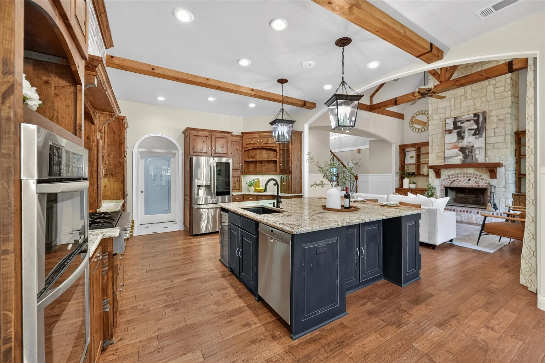 Kitchen featuring wood-finish flooring, stainless steel appliances, granite countertops, wood cabinetry, and exposed ceiling beams