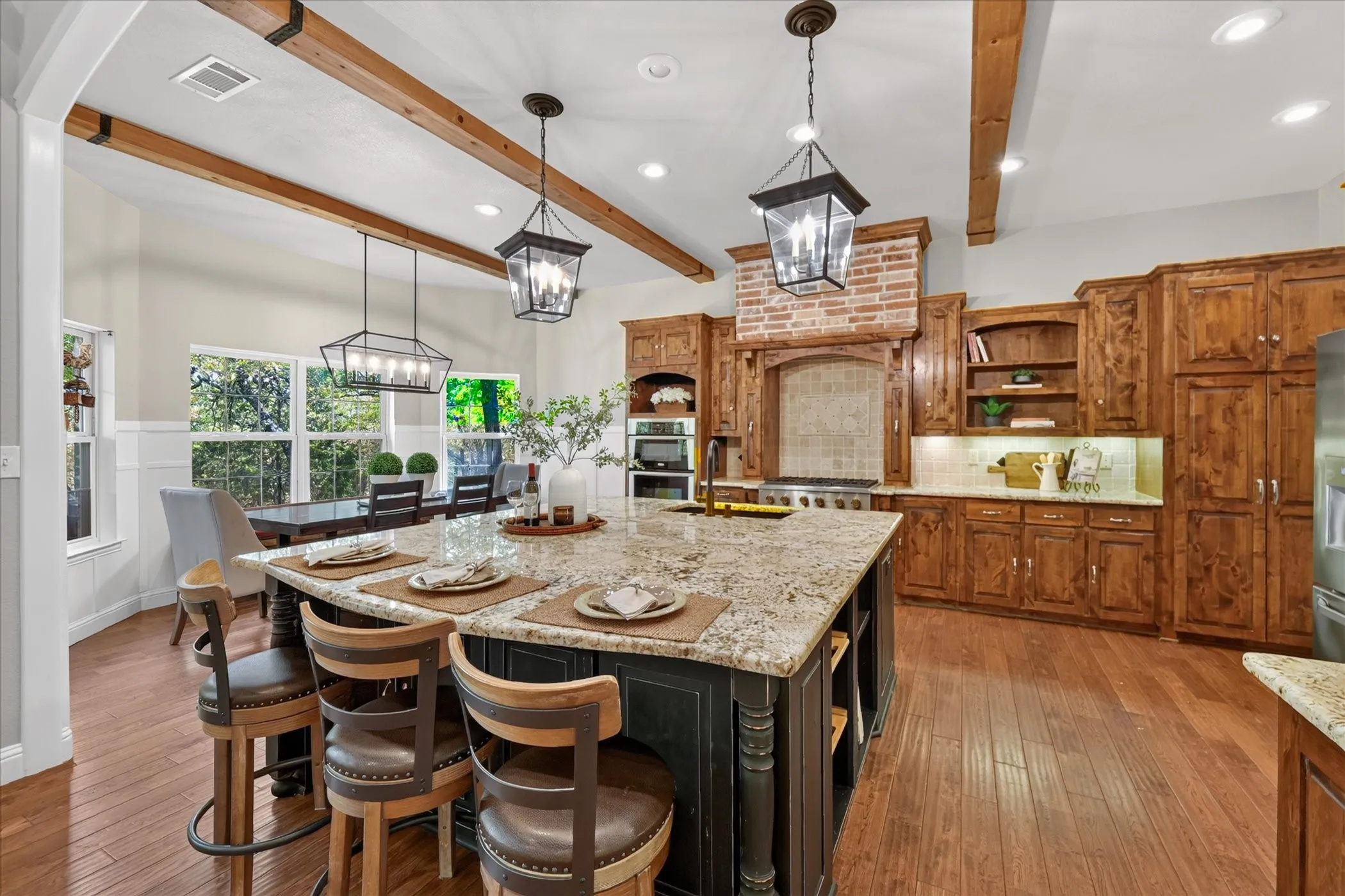 Spacious kitchen featuring an expansive center island with seating, wood-finish flooring, exposed ceiling beams, and integrated stainless steel appliances