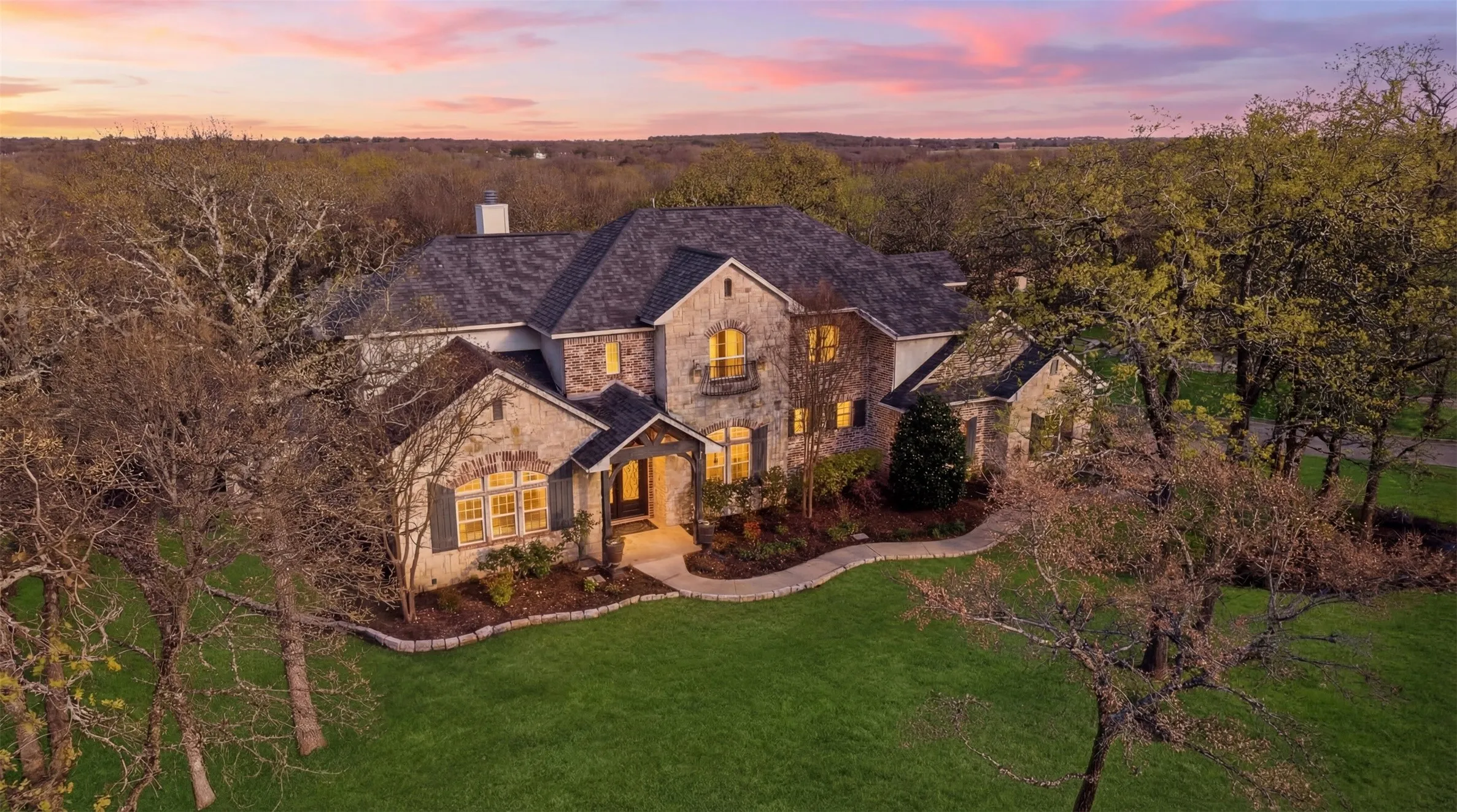 Stone facade residence featuring a multi-gabled shingle roof, established landscaping, and a winding pathway