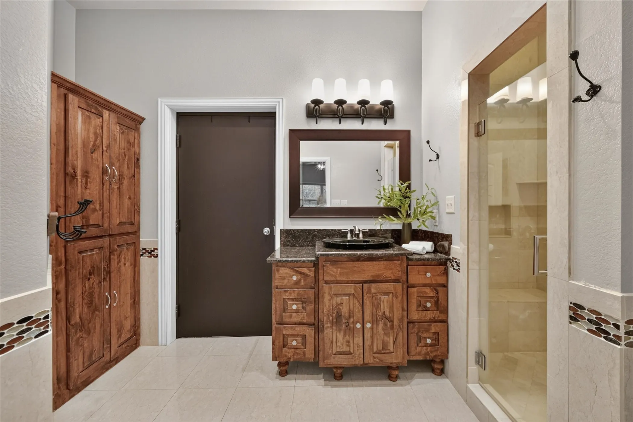 Bathroom featuring a glass-enclosed shower, wood vanity with basin sink, wood-finish cabinetry, and tiled flooring