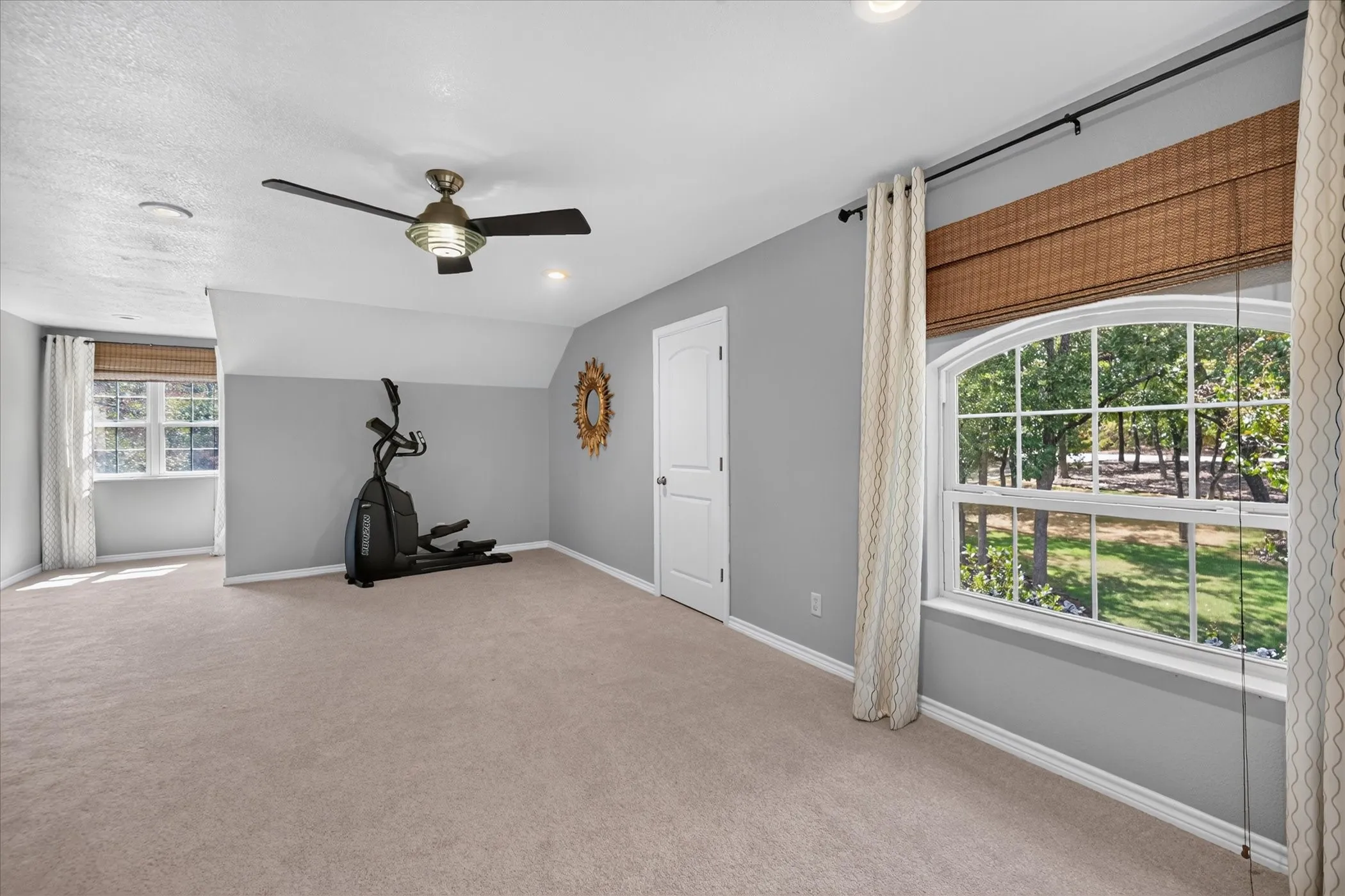 Expansive carpeted room featuring an arched window, a secondary window, a ceiling fan, and recessed lighting