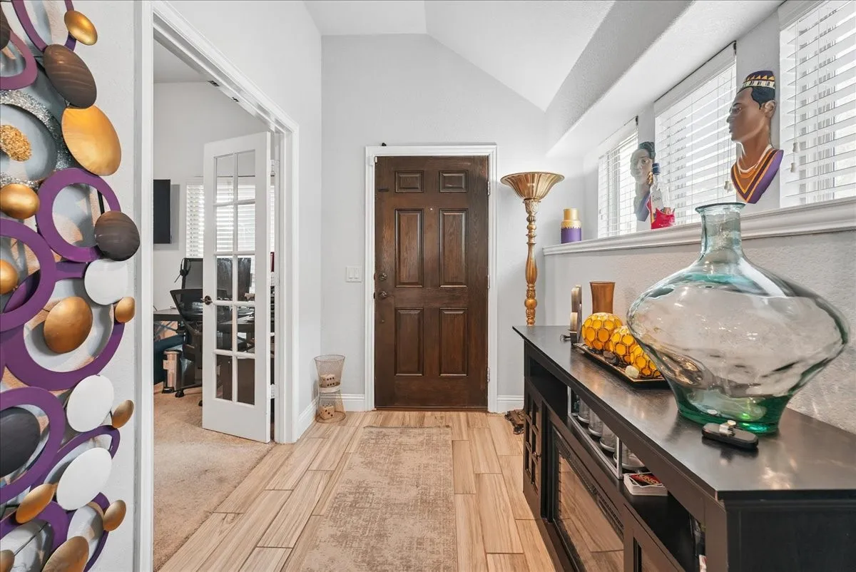 Wood-finish flooring, dark wood entry door, vaulted ceiling, white interior paint, and french doors