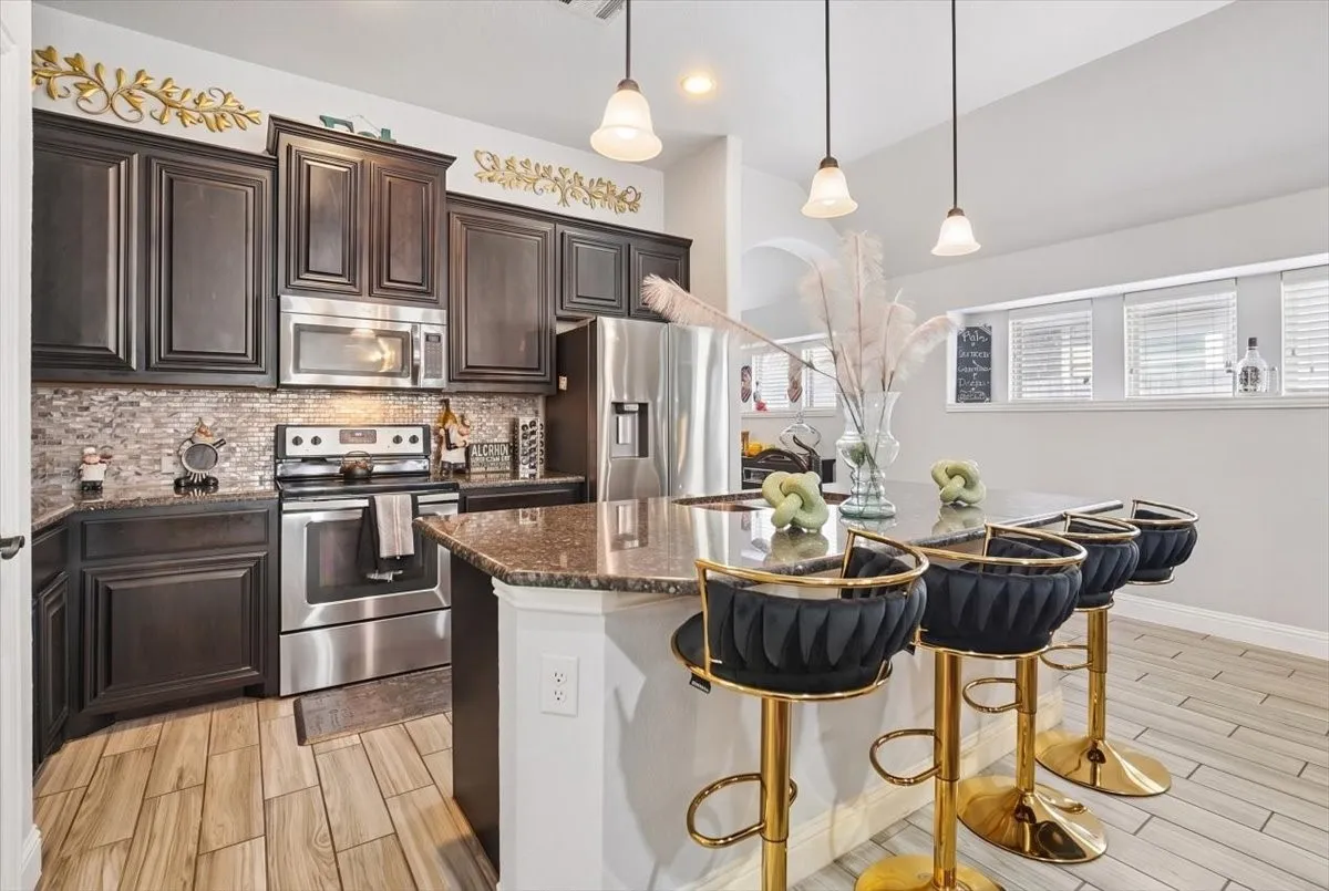Kitchen featuring wood-finish flooring, dark wood cabinetry, stainless steel appliances, a mosaic tile backsplash, and a breakfast bar with pendant lighting