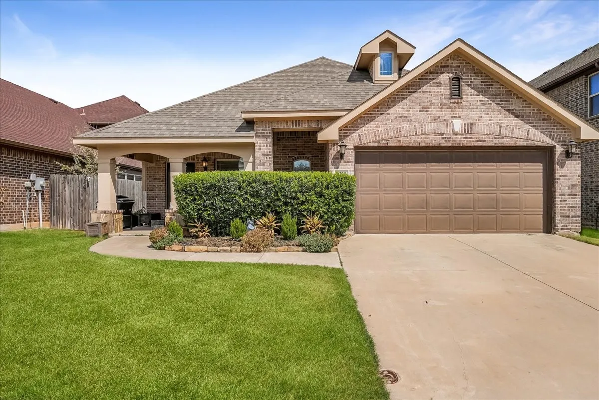 Brick exterior with a covered porch, attached garage, concrete driveway, and dormer window