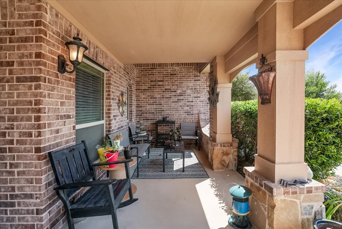 Covered front porch featuring brick and stone accent columns, a concrete floor, and brick exterior walls
