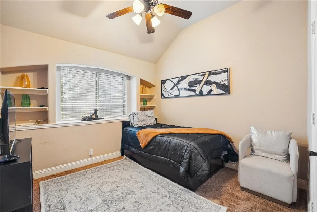 Vaulted ceiling with a ceiling fan light fixture, built-in shelving, window with blinds, and carpet flooring