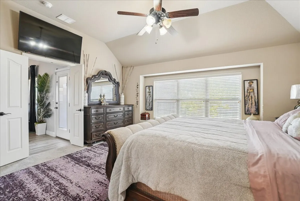 Vaulted ceiling with a ceiling fan, wall-mounted television, large window with blinds, and French doors