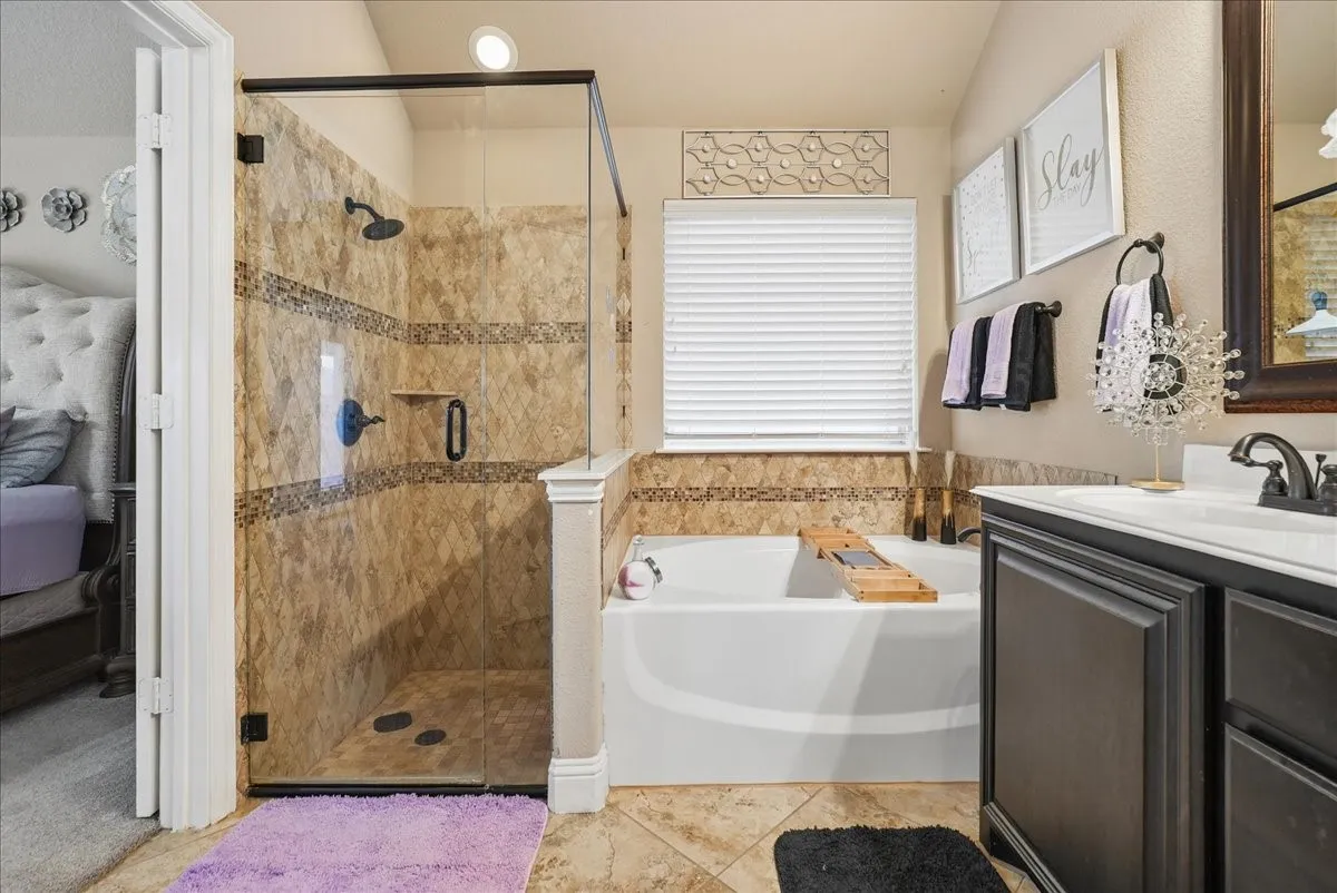 Walk-in shower with glass enclosure, separate soaking tub, vanity with integrated sink, wood-finish cabinetry, and tiled flooring
