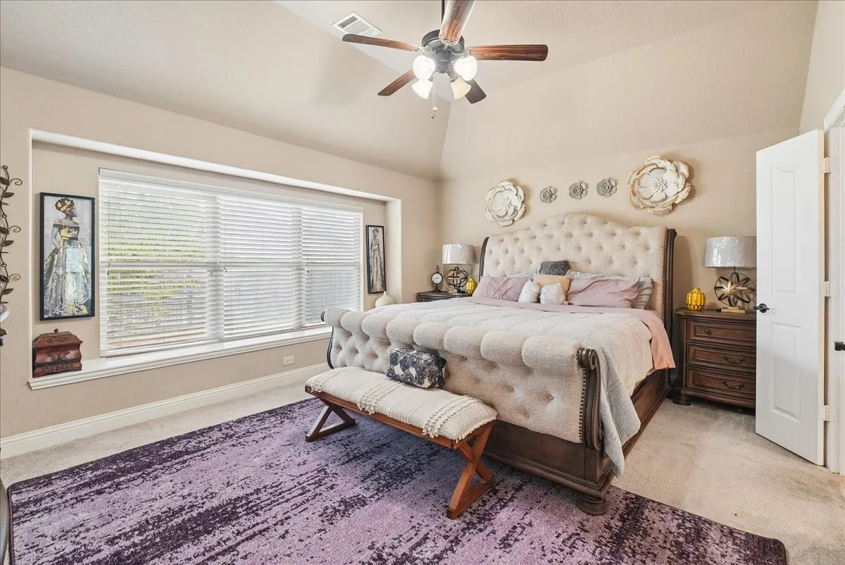 Vaulted ceiling, ceiling fan with integrated lighting, large window with blinds, light wall color, and carpeted flooring