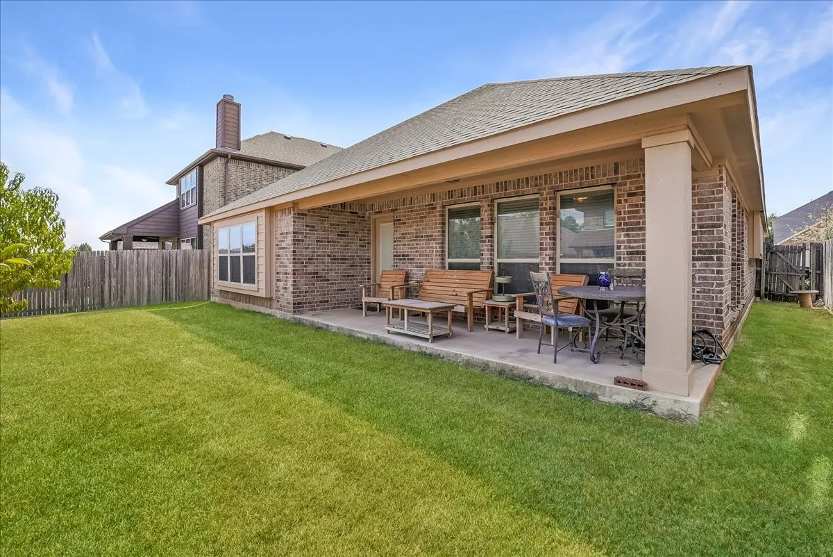 Expansive backyard featuring a manicured lawn, a full brick exterior, a covered patio, and multiple windows