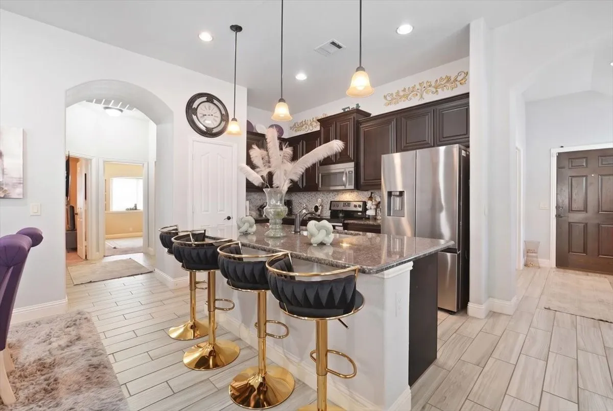 Kitchen featuring dark wood-finish cabinetry, stainless steel appliances, a center island with a stone countertop, and pendant lighting