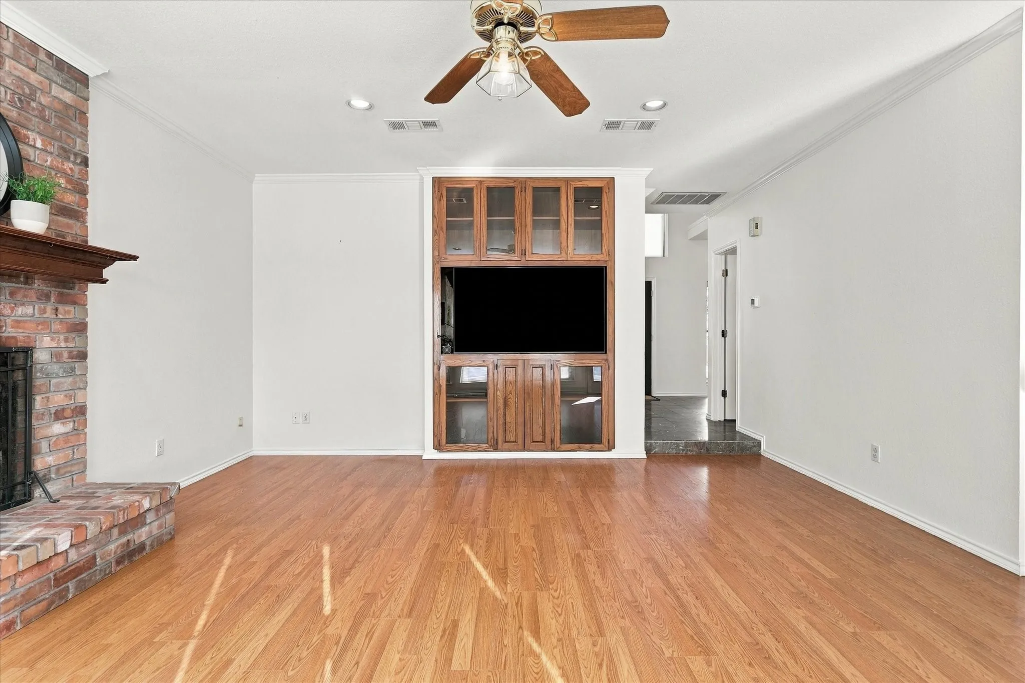 Wood-finish flooring, brick fireplace with wood mantel, built-in entertainment center, ceiling fan, recessed lighting