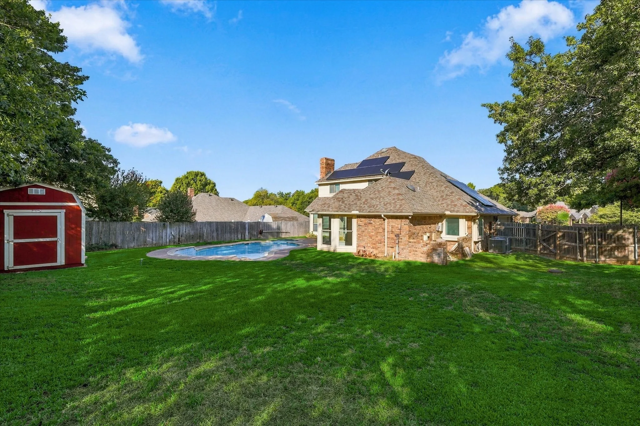 Expansive yard with a swimming pool, brick exterior, and solar panels on the roof