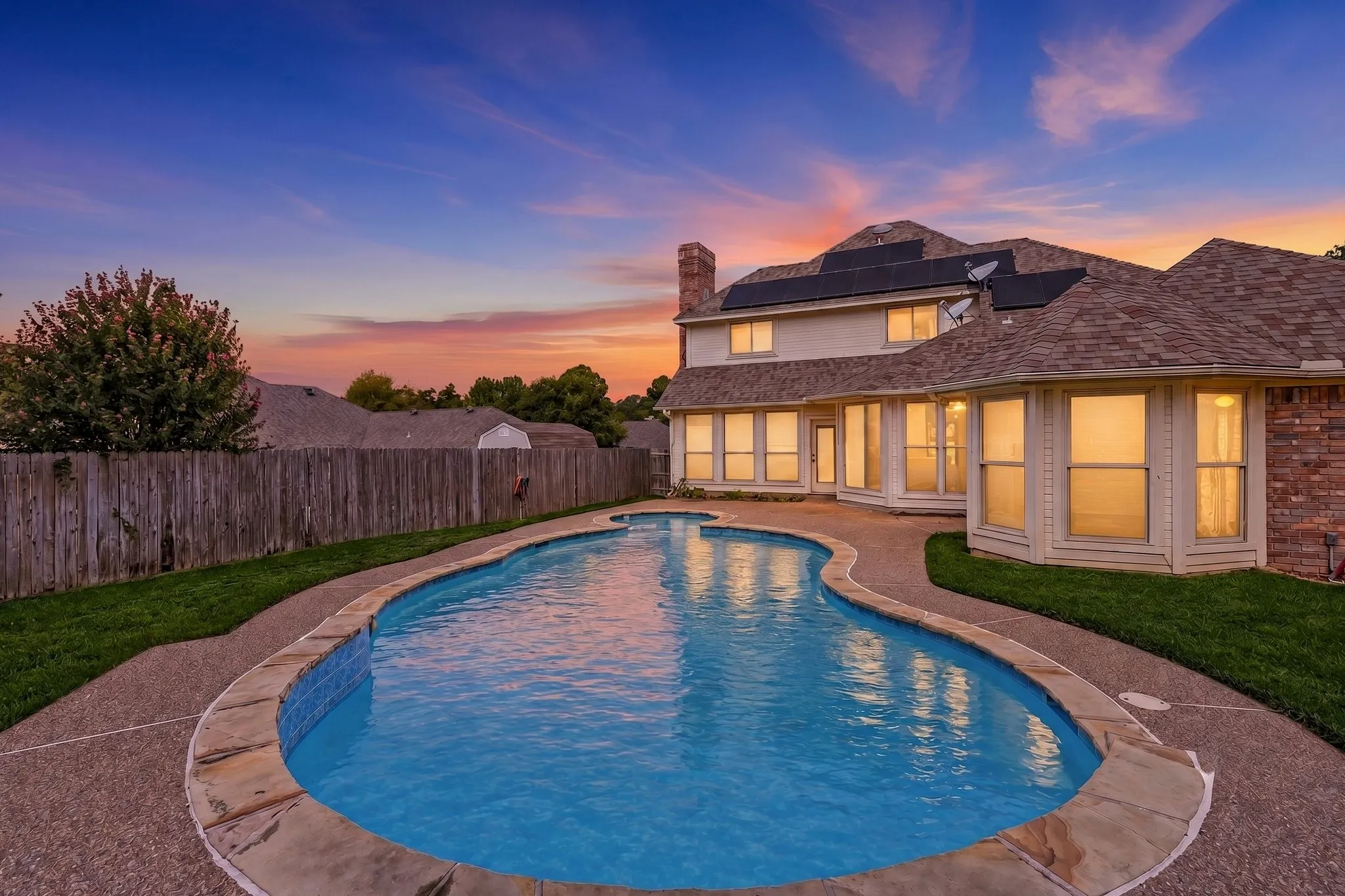 Curved swimming pool with stone coping, surrounded by a concrete patio and green lawn