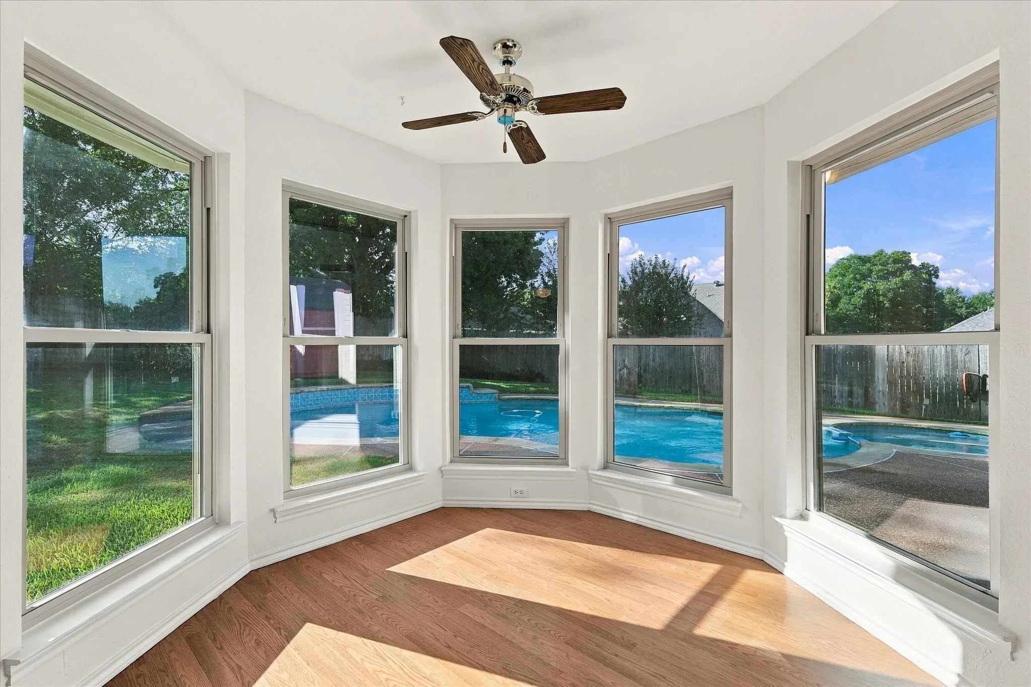 Bay window with five individual windows, wood-finish flooring, white walls, and a ceiling fan