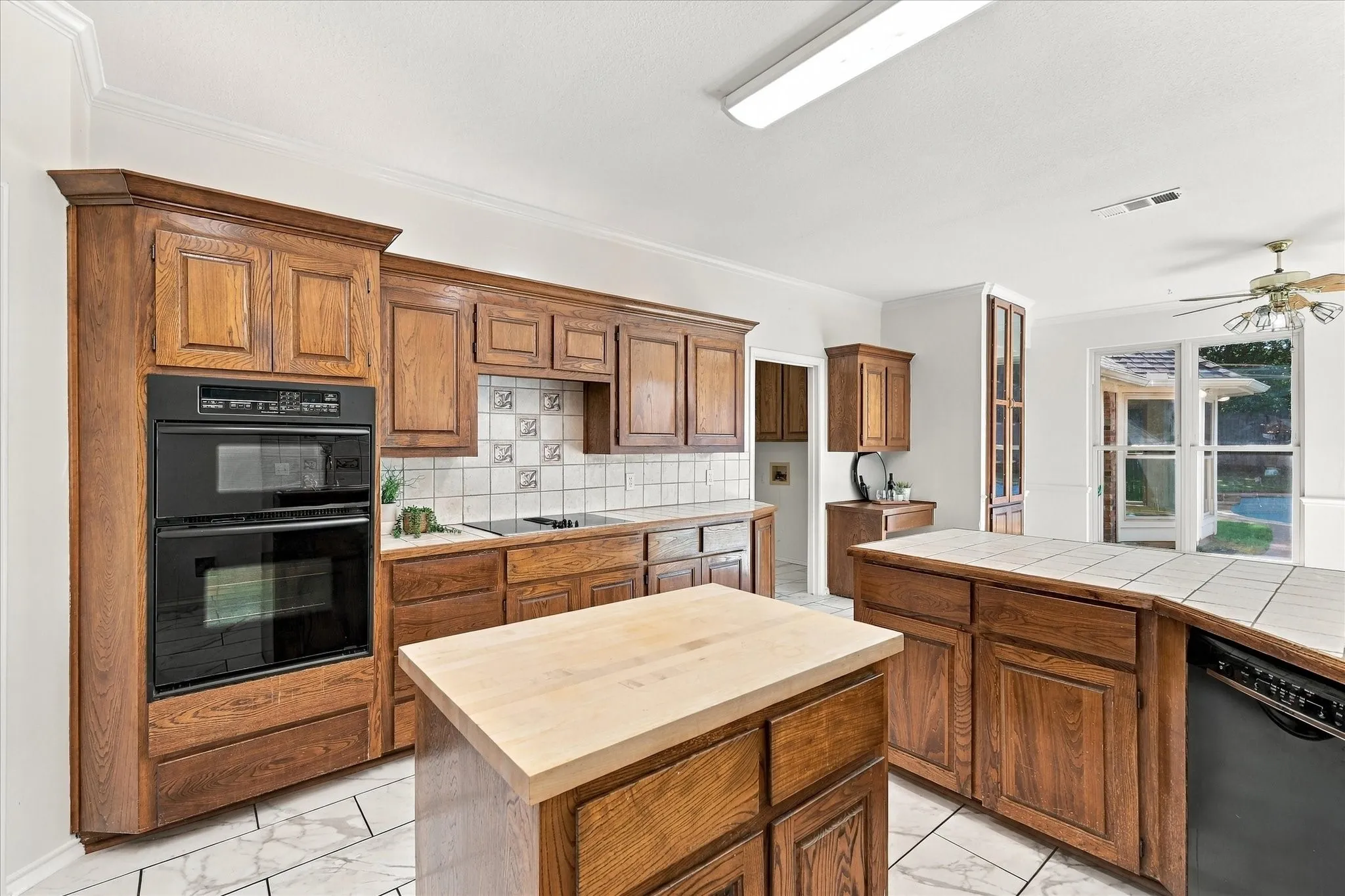 Spacious kitchen featuring wood-finish cabinetry, tile flooring, built-in double ovens, a central island with a wood-finish top, and a secondary island with a tiled countertop