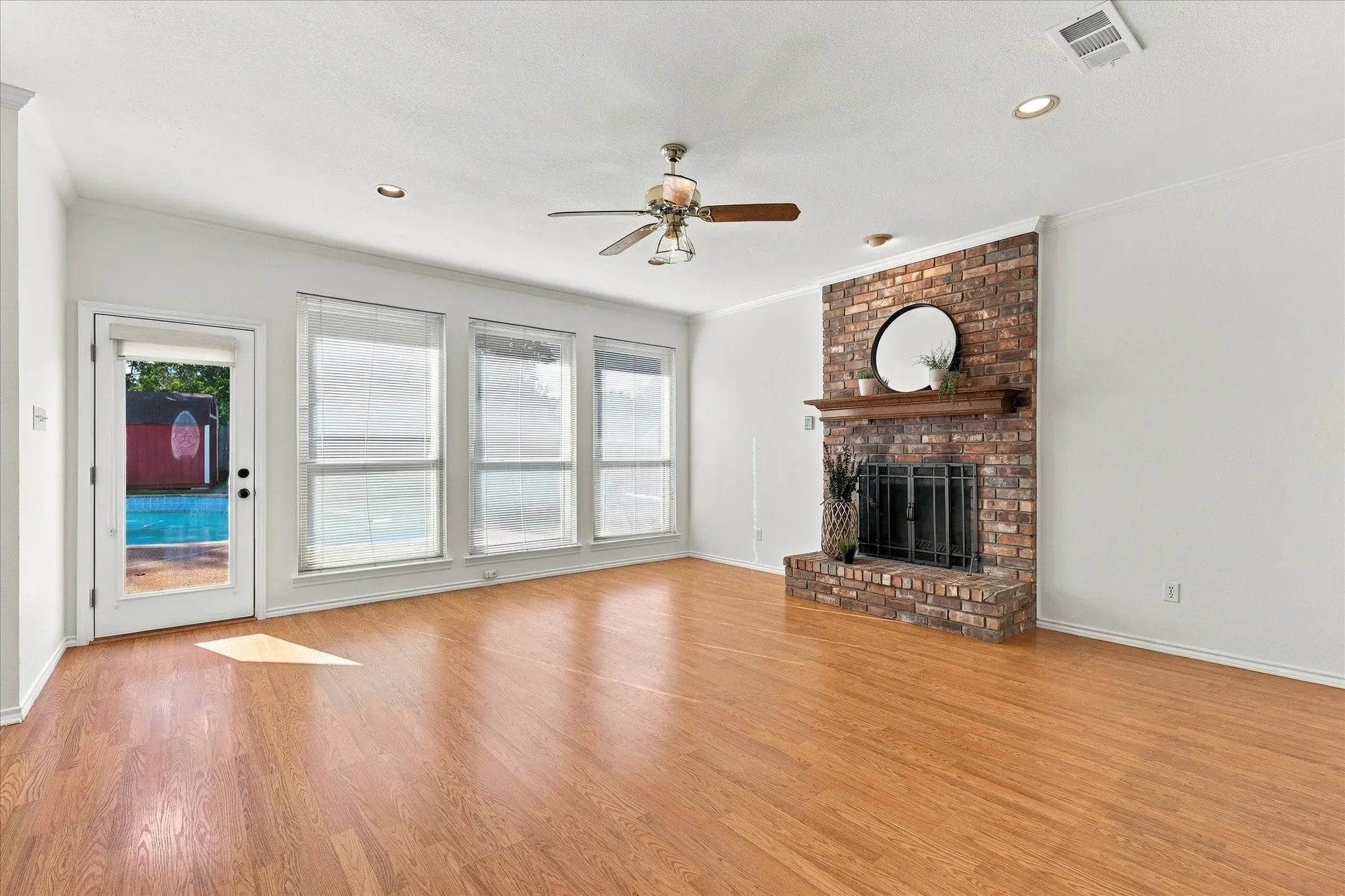 Hardwood-style flooring throughout, brick fireplace with a wood mantle, three panel windows, glass-paneled door, and a ceiling fan