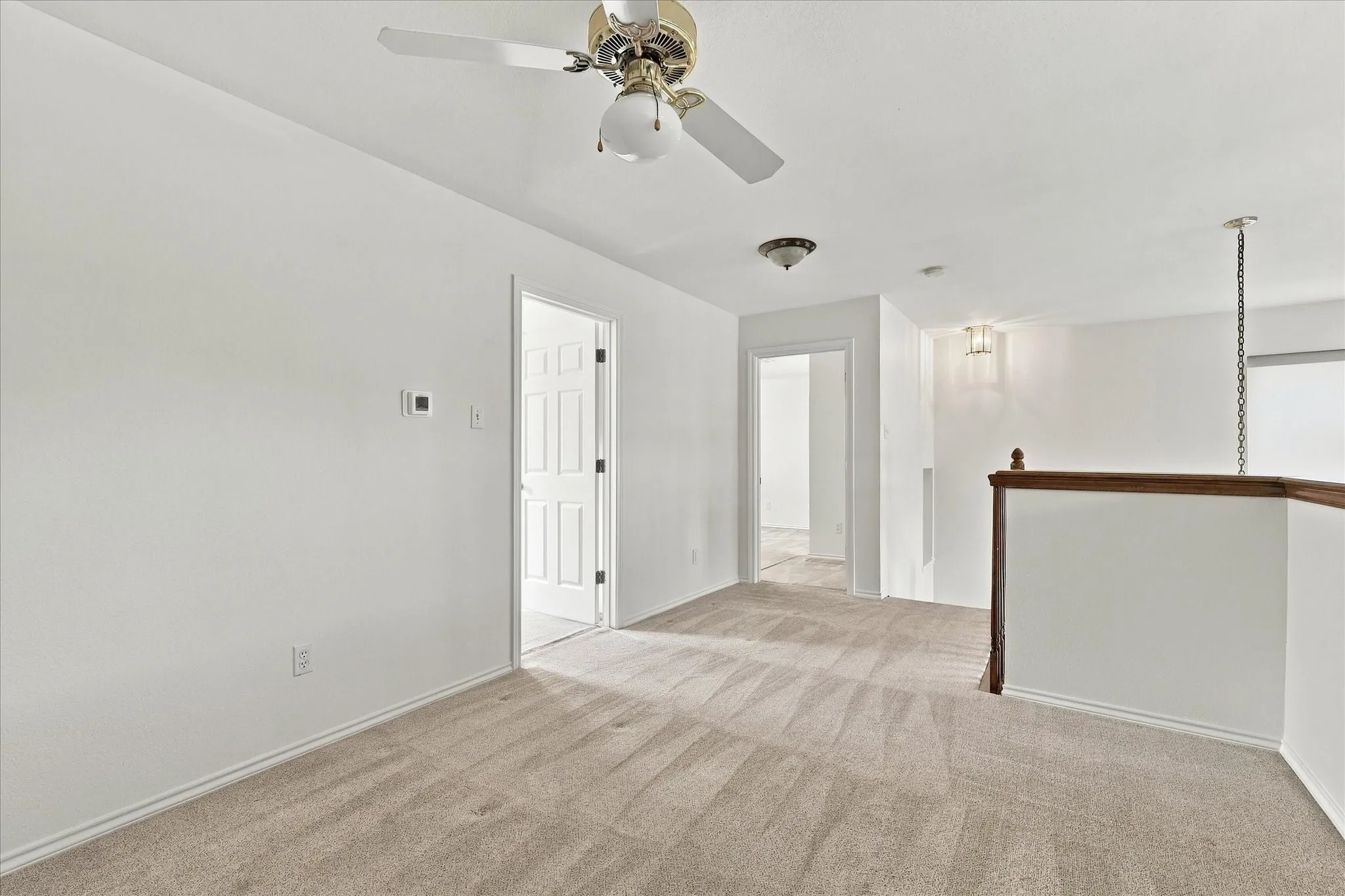 Carpeted flooring, white walls, ceiling fan, flush-mount lighting, and wood-toned handrail