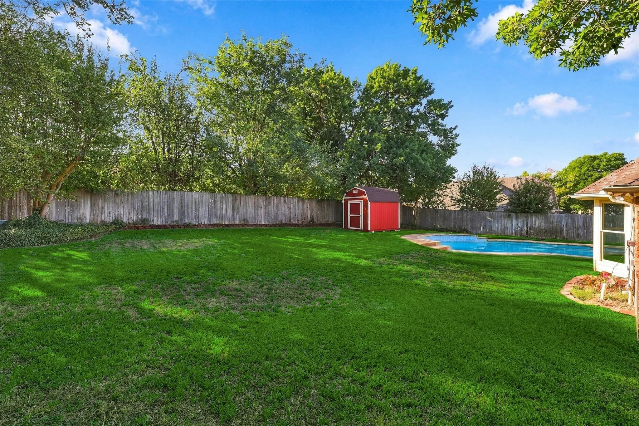Expansive green lawn with a swimming pool, wood privacy fence, and a red storage shed