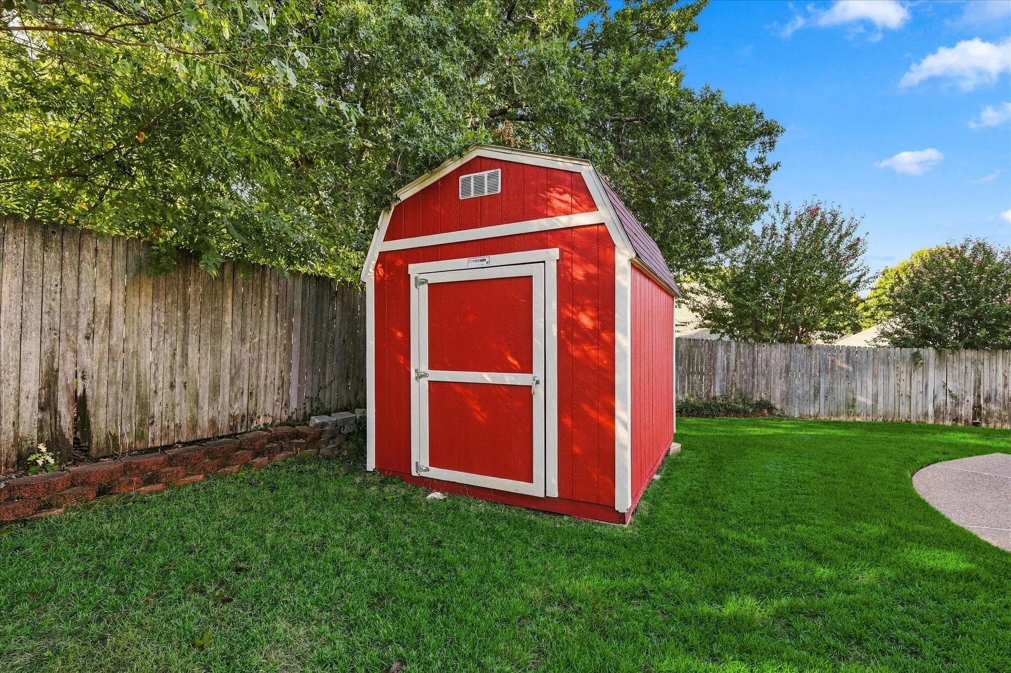 Tuff Barn brand Garden Barn Red-painted storage shed with white trim, set on a green lawn