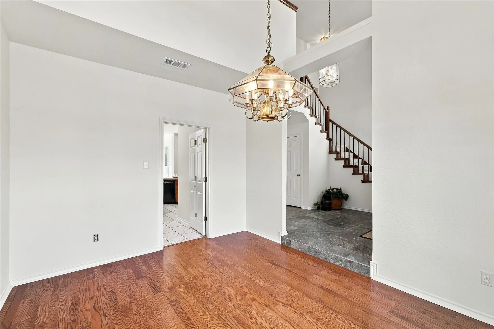 Wood-finish flooring, overhead chandelier, staircase with wooden banister, and vaulted ceiling