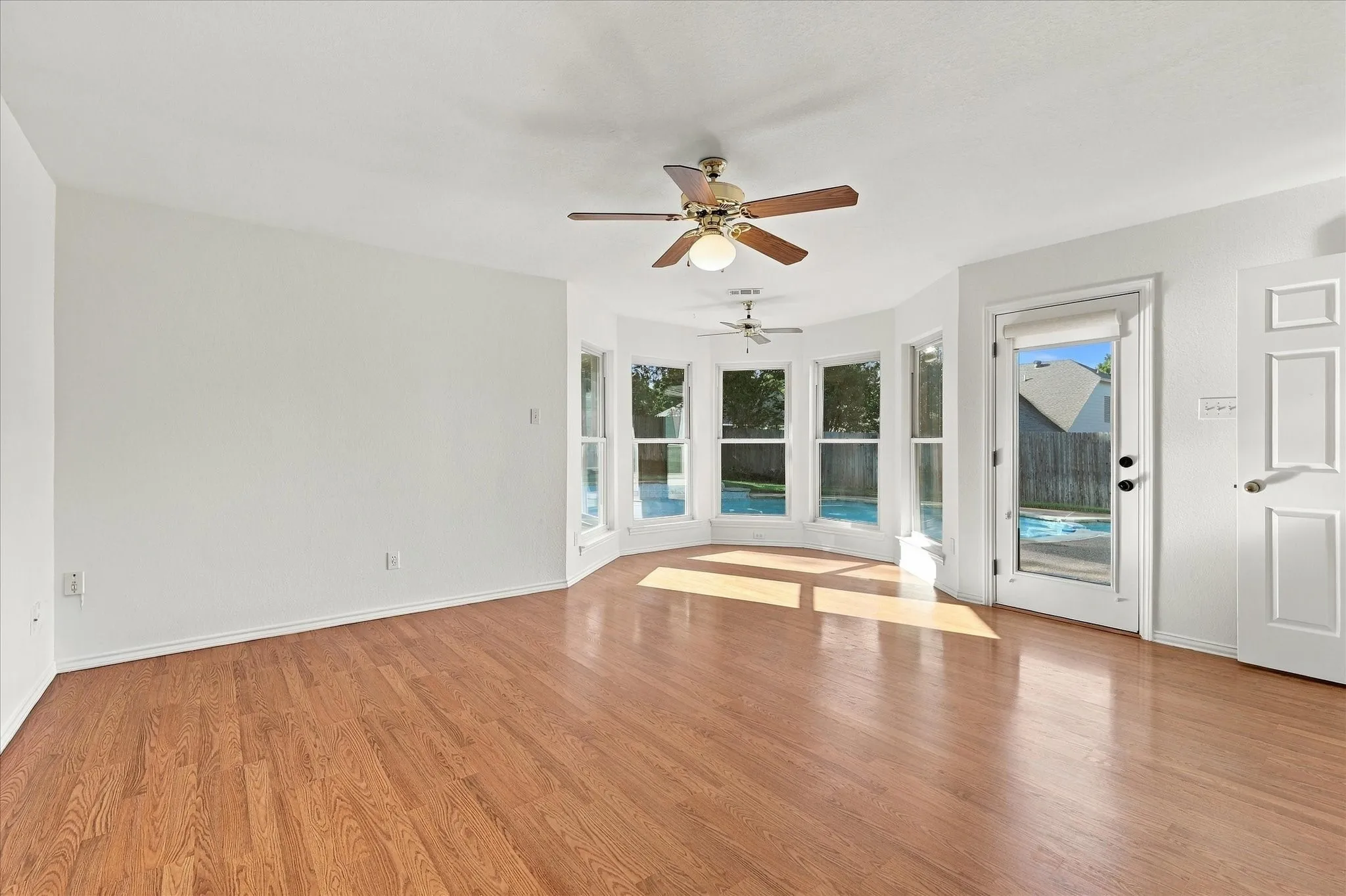 Wood-finish flooring, multiple ceiling fans, a bay window with multiple panes, a white paneled door, and a glass-paneled exterior door