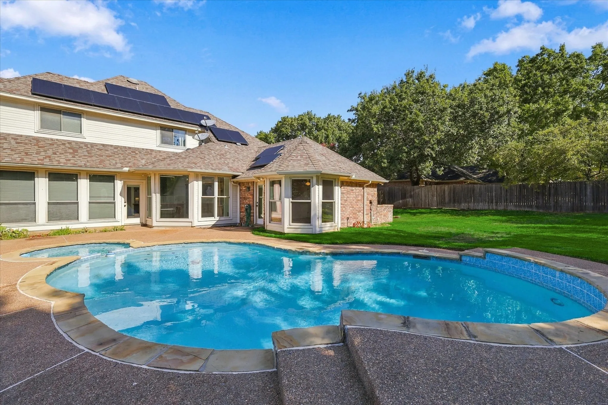 In-ground swimming pool with integrated non-heated spa, expansive paver patio, paid for solar panels, and a manicured lawn
