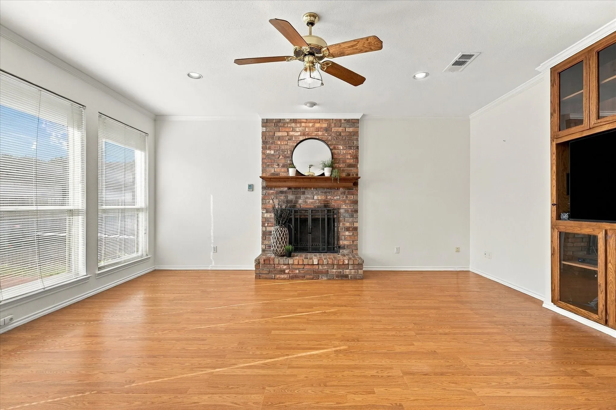 Brick-clad fireplace with a wood mantel, wood-finish flooring, and recessed lighting