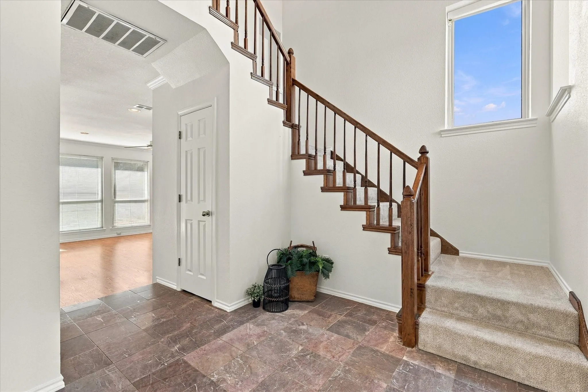 Entryway featuring dark-toned tile flooring, a carpeted staircase with wood handrails, and a large window providing natural light